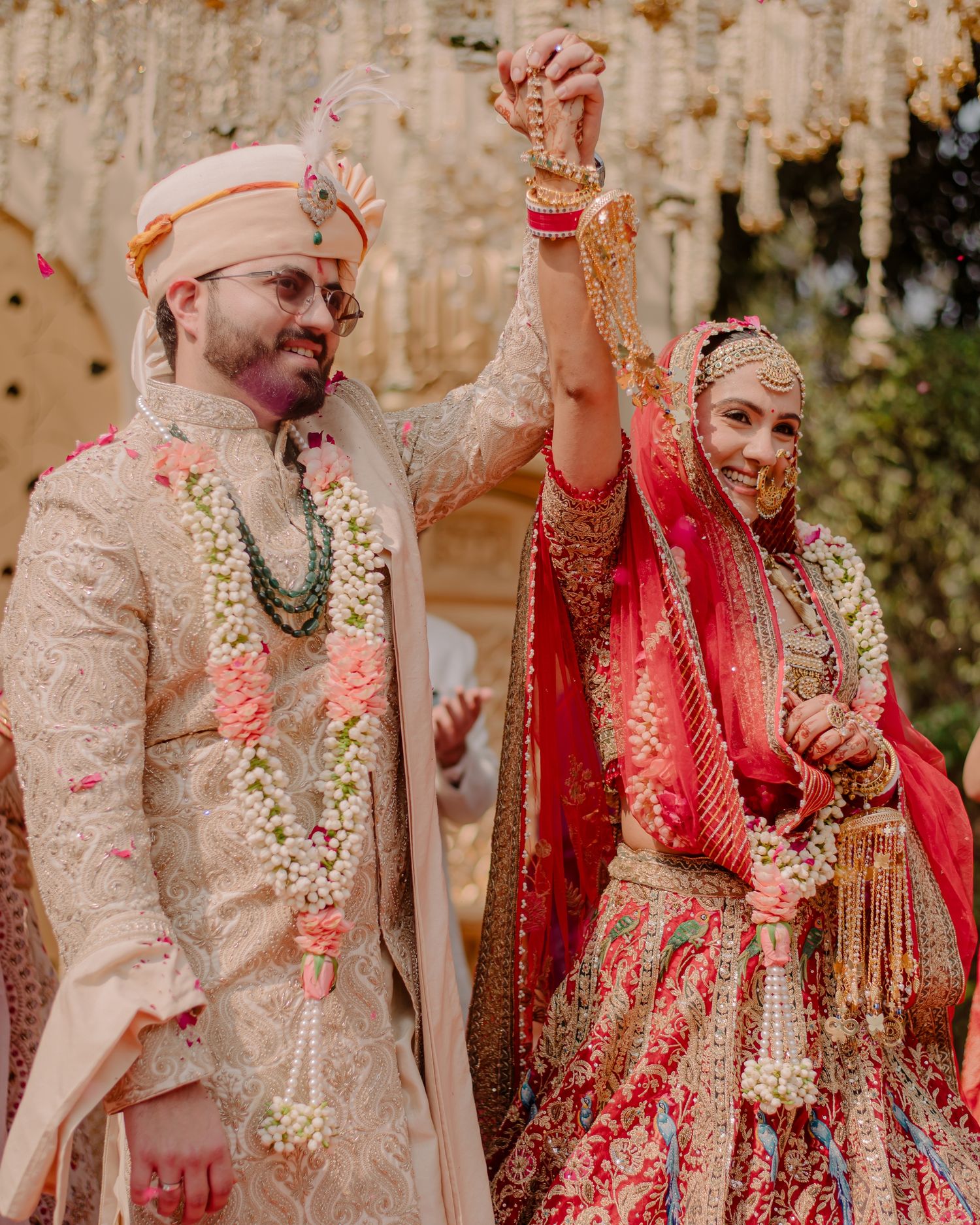 Joyful Indian bride in red lehenga and groom in cream sherwani celebrate their wedding ceremony together.