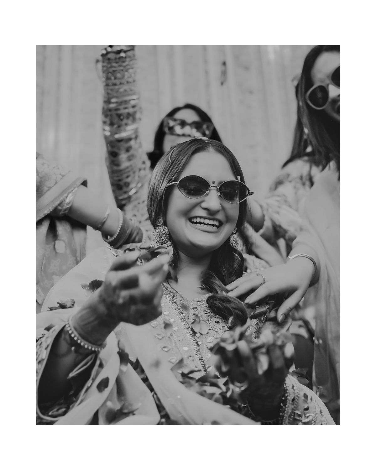 Black and white portrait of bride laughing while being showered with flower petals.