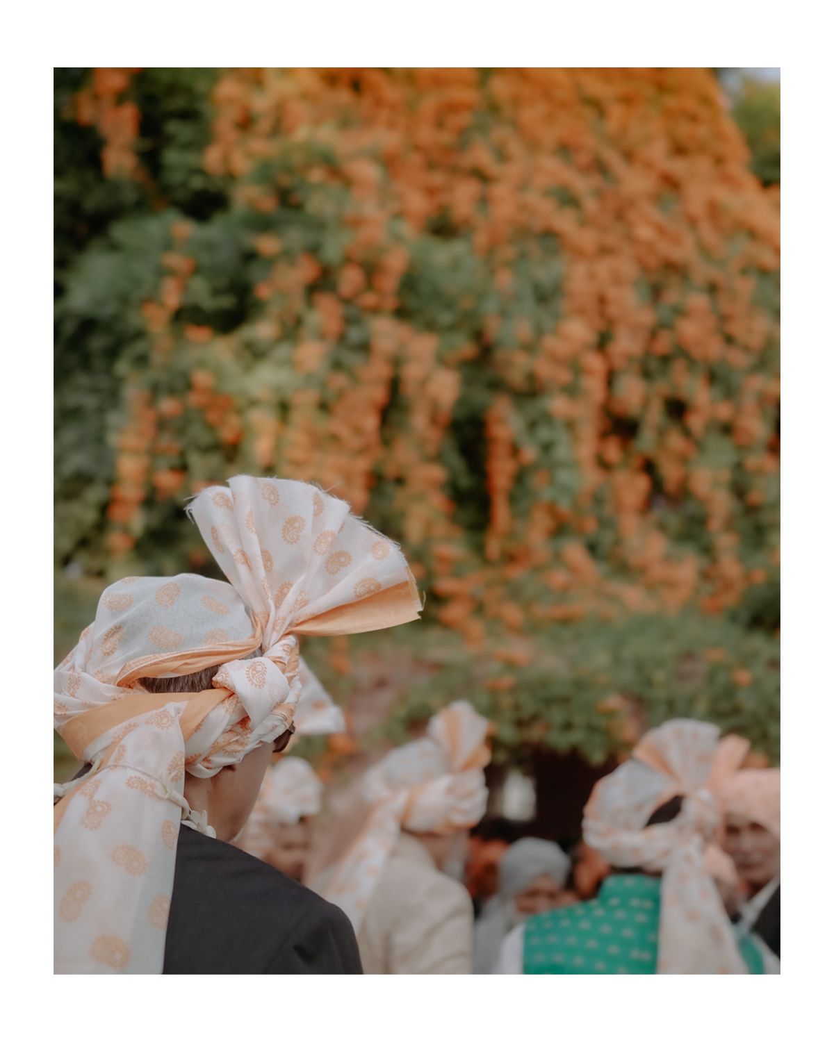 Decorative white bows adorn chairs at an outdoor wedding ceremony with autumn foliage in the background.