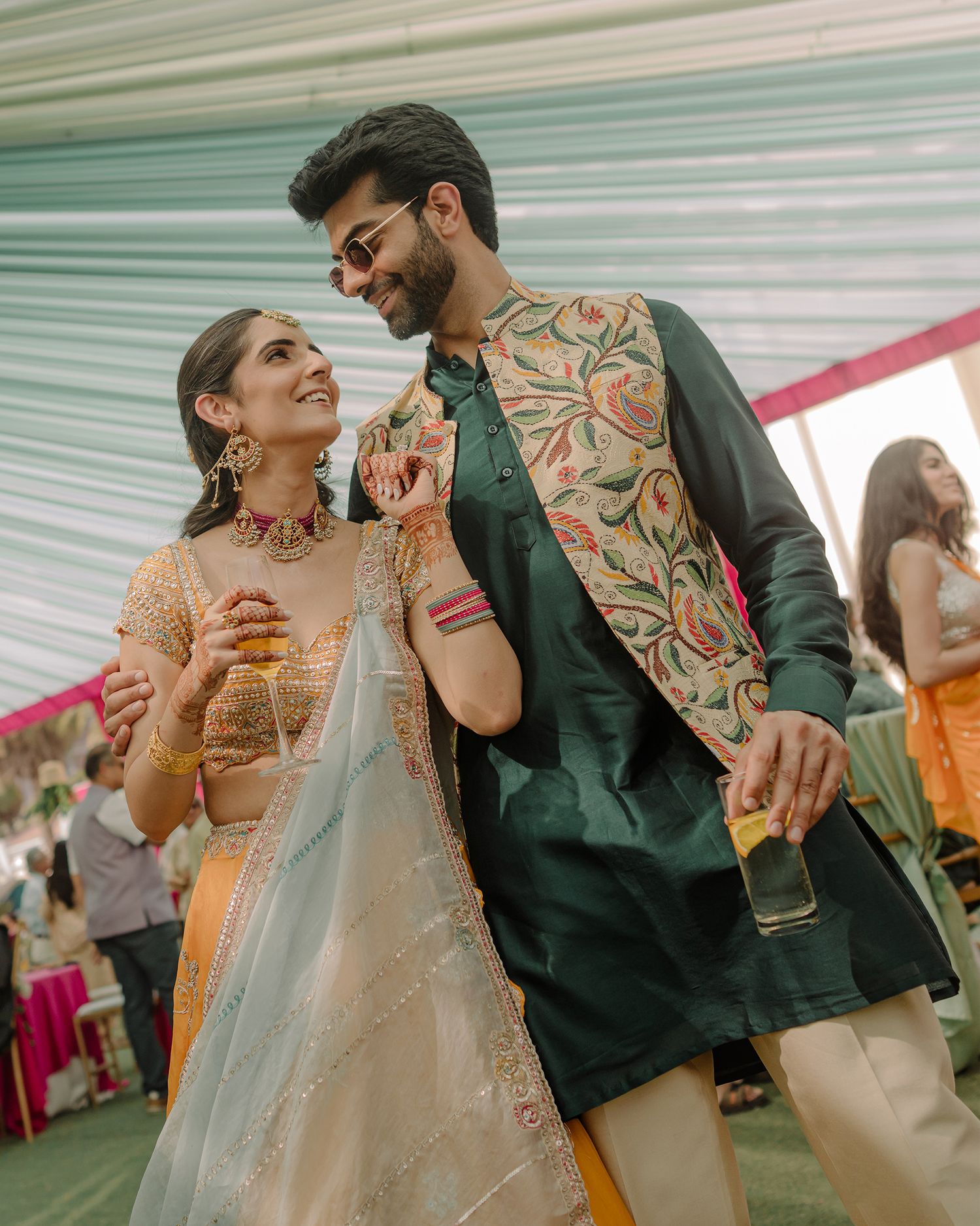 Couple in traditional Indian attire smiling at each other during a wedding celebration, woman in lehenga, man in kurta.
