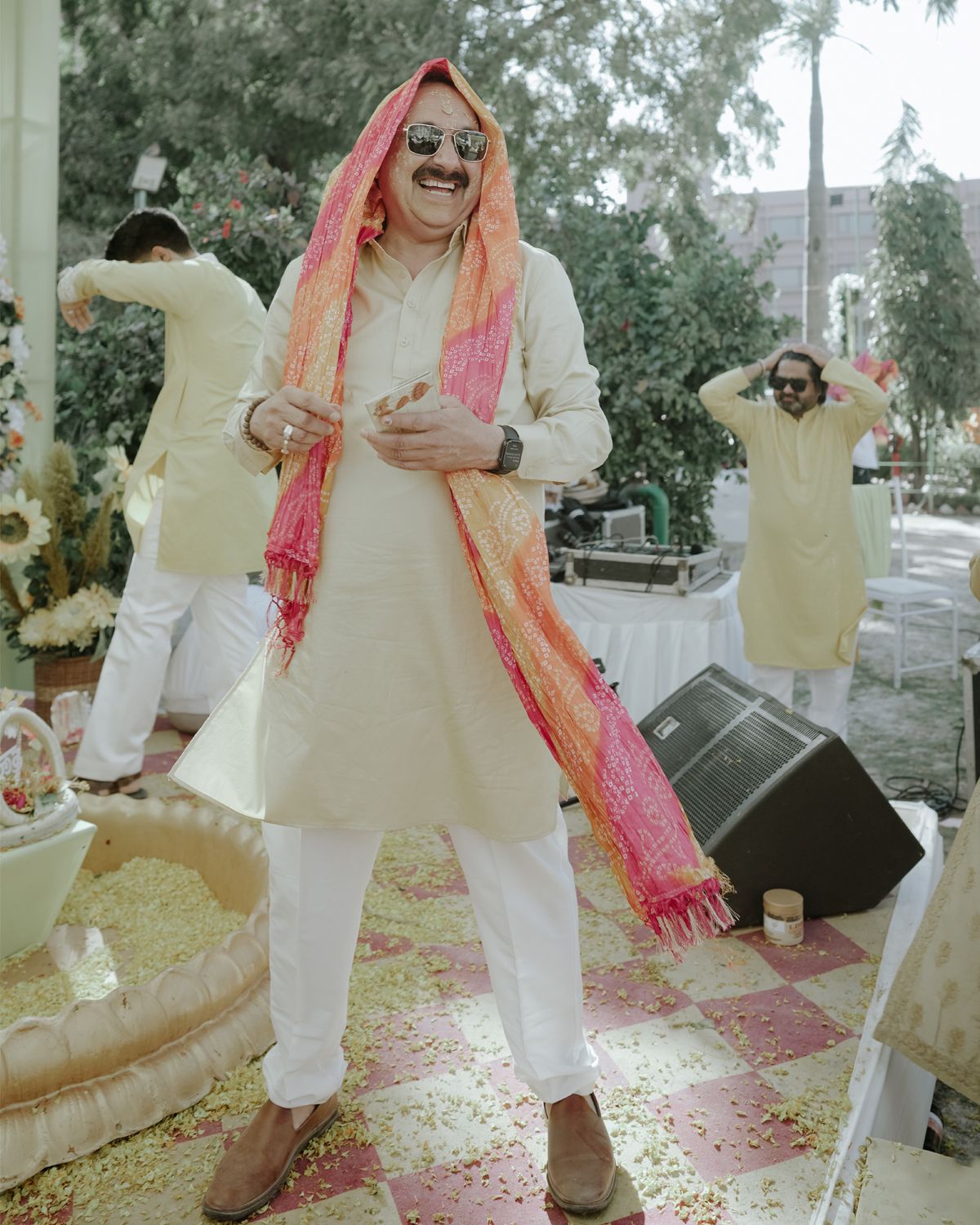 Guest in cream-colored kurta and pink scarf dances at an Indian wedding celebration.