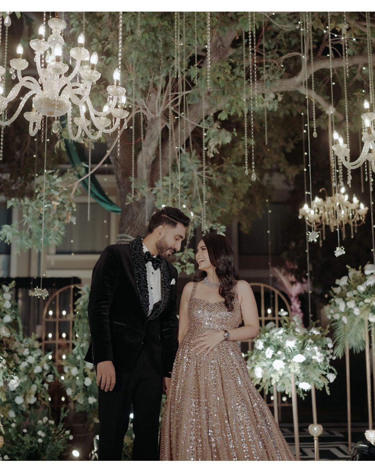 Couple shares intimate moment beneath crystal chandeliers and hanging garden decorations.