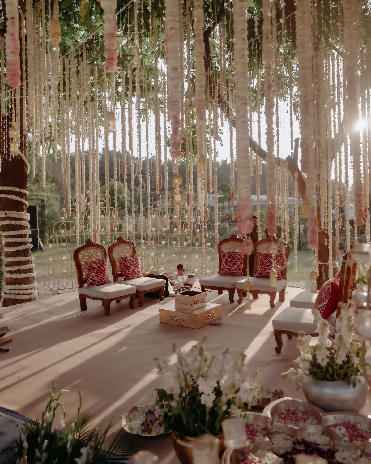 Elegant wedding lounge area with vintage red velvet chairs, hanging crystal decor and floral arrangements in a forest setting.
