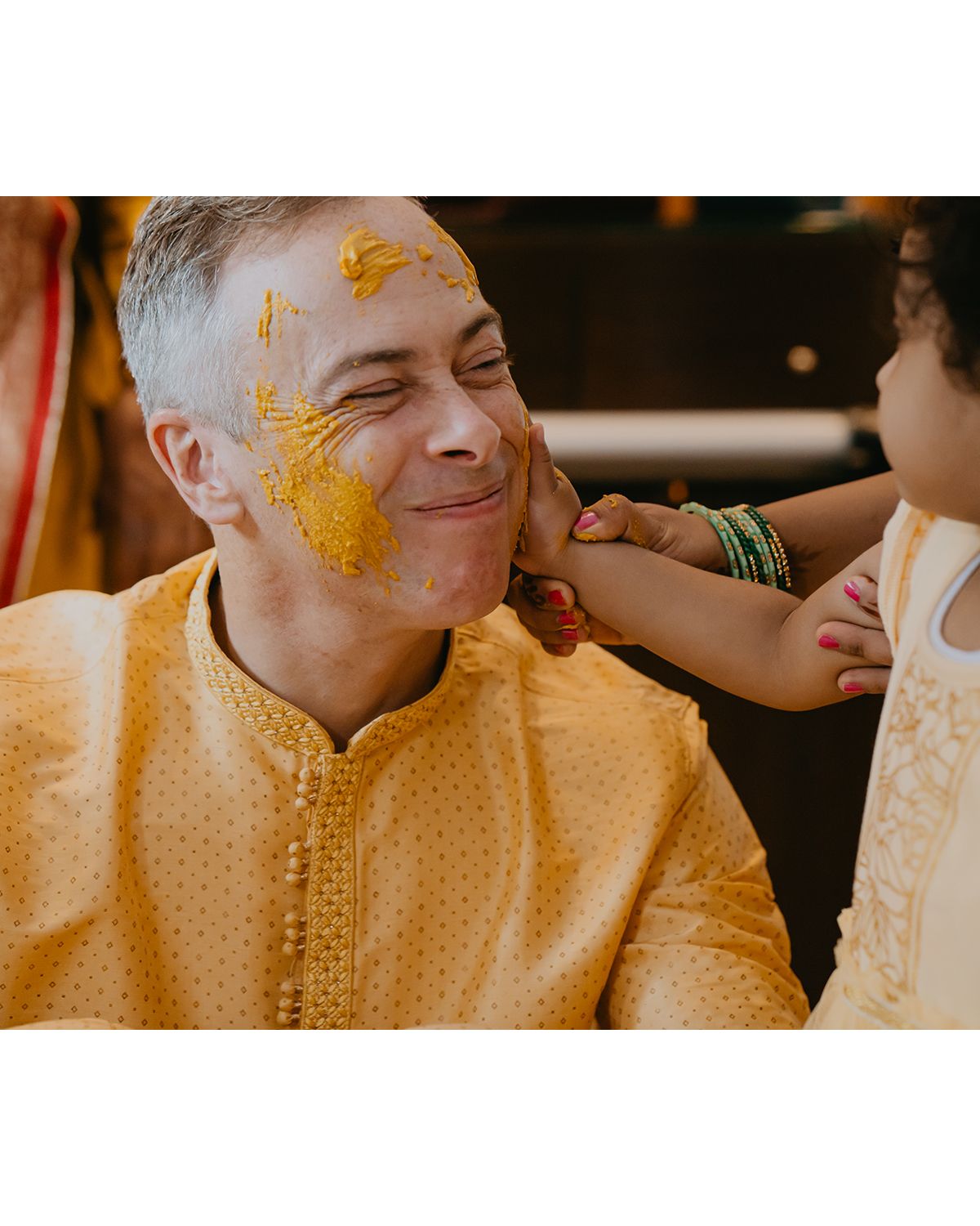 Person in yellow traditional attire having turmeric applied during a Haldi ceremony.