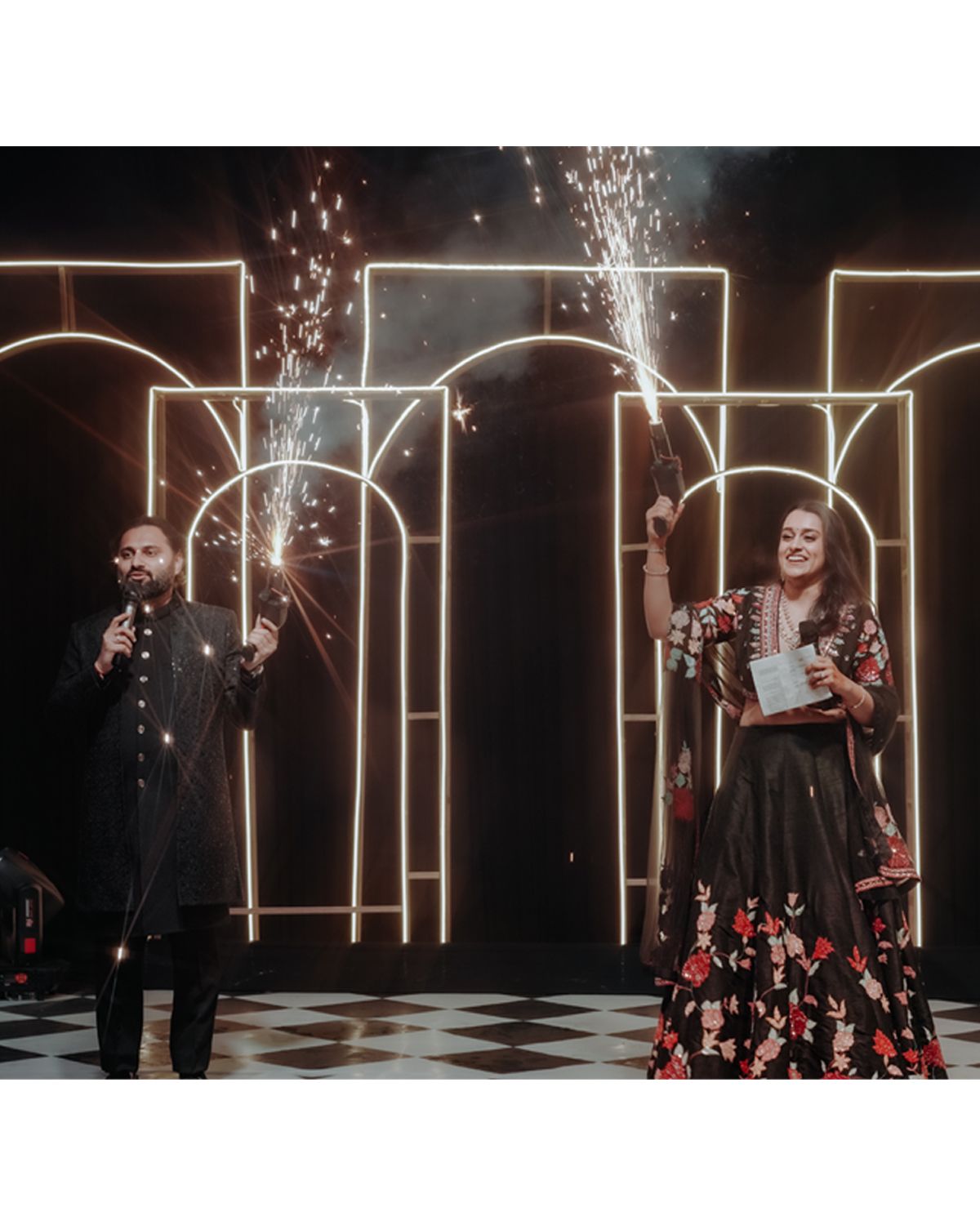 Performers on stage with illuminated geometric arch backdrop and sparkler effects during a theatrical live show.