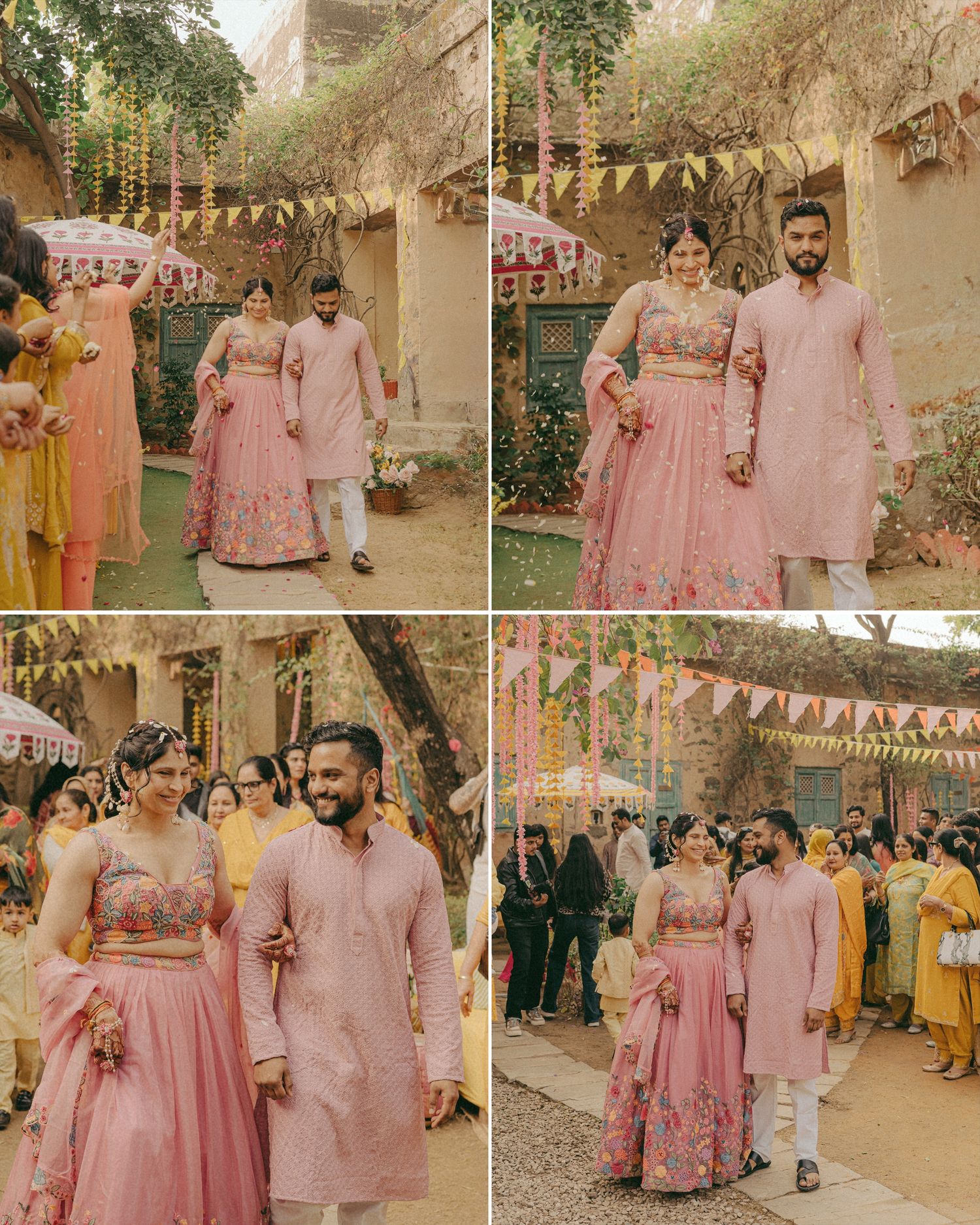Couple in matching pink Indian wedding attire walk together at an outdoor mehendi ceremony with floral decorations.