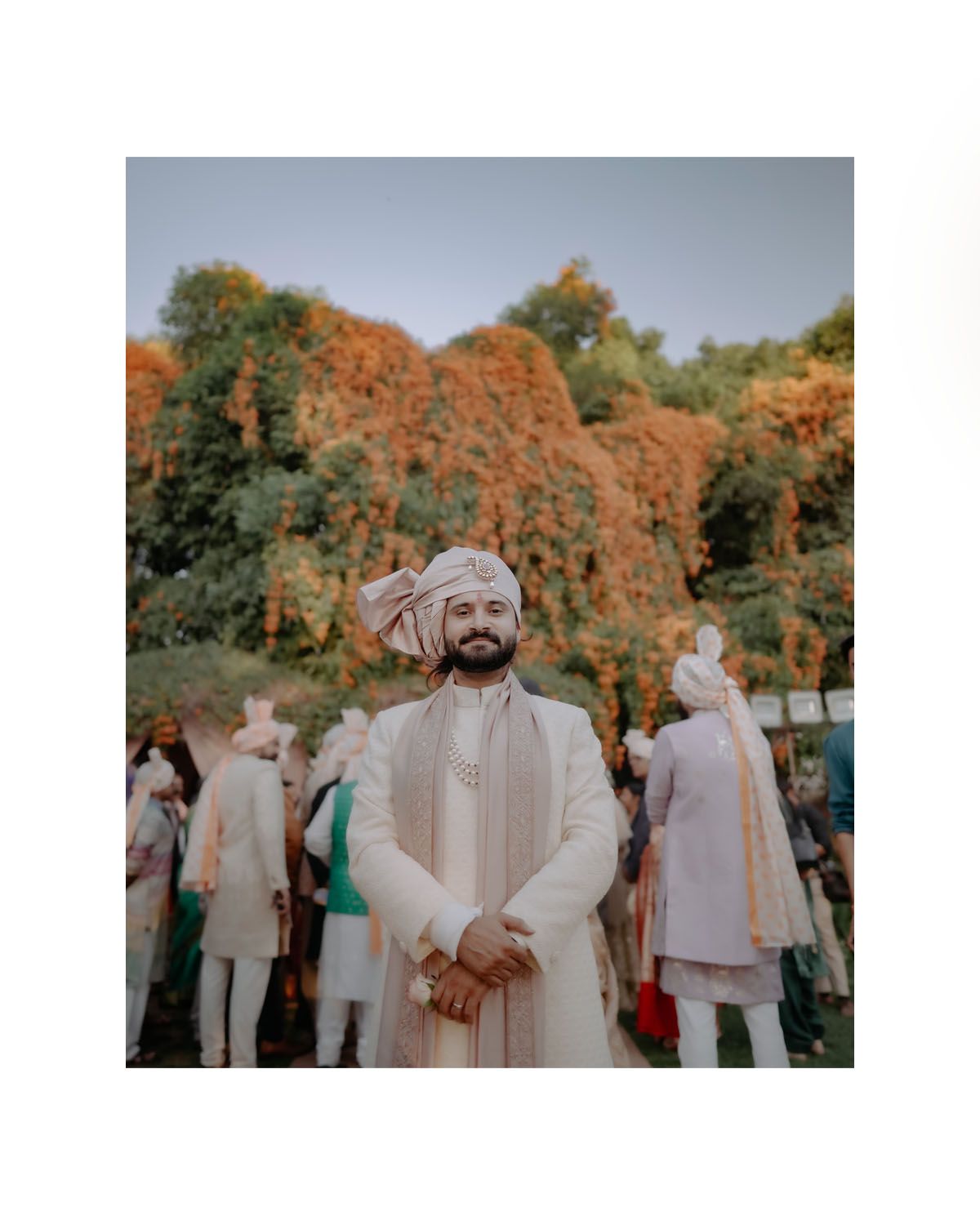 Traditional outdoor Indian wedding gathering with autumn foliage and guests in cultural attire against orange trees.