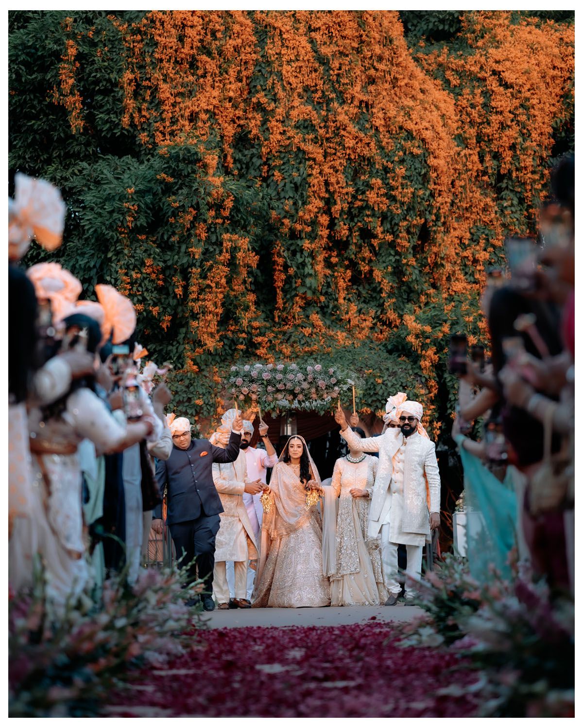 Wedding ceremony procession walking under stunning orange autumn foliage archway with guests lining the path.