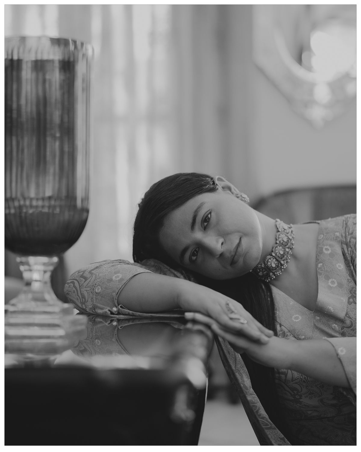 Vintage black and white portrait of someone in elegant dress reclining near a glass goblet.
