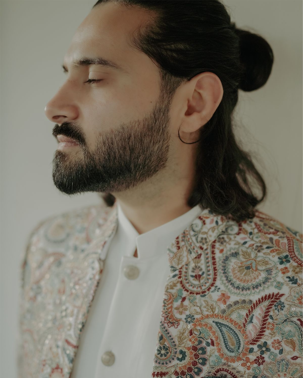 Profile view of someone wearing a white mandarin collar shirt and ornate paisley jacket with their eyes closed.