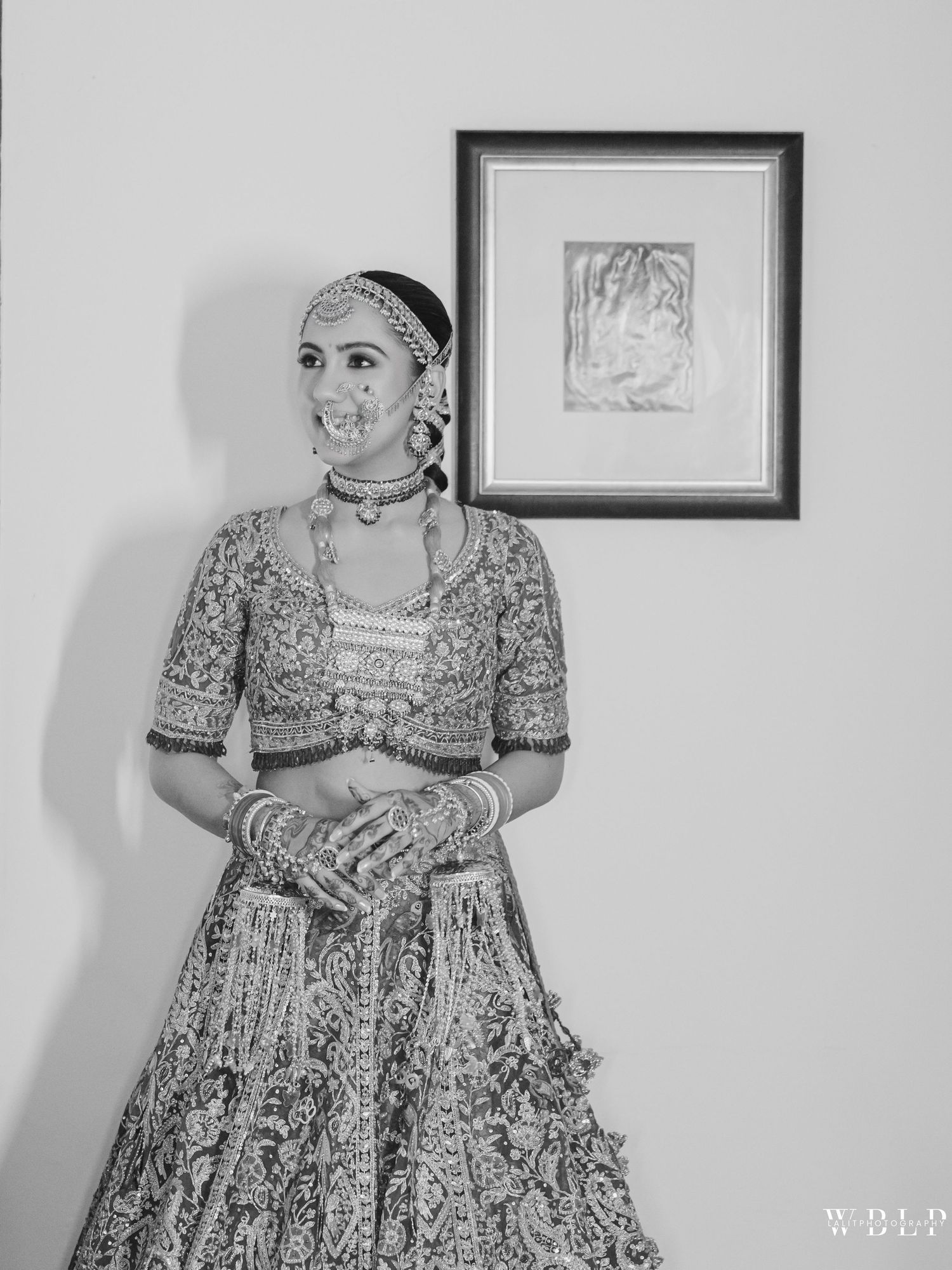 Black and white portrait of an Indian bride in traditional lehenga and jewelry posing elegantly indoors.