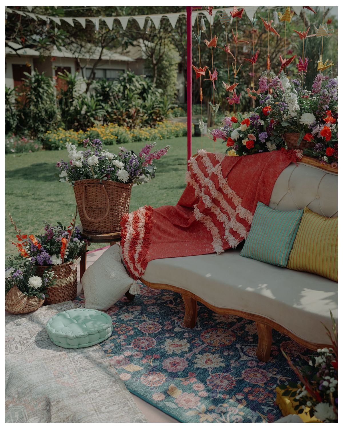 Cozy outdoor patio seating with colorful floral planters, cushions, and a vintage sofa draped with a red striped throw blanket.