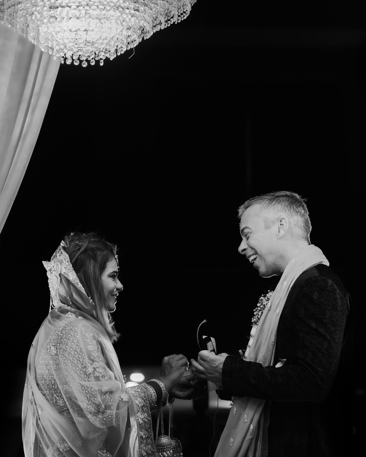 Black and white photo of a ring exchange ceremony under a crystal chandelier.