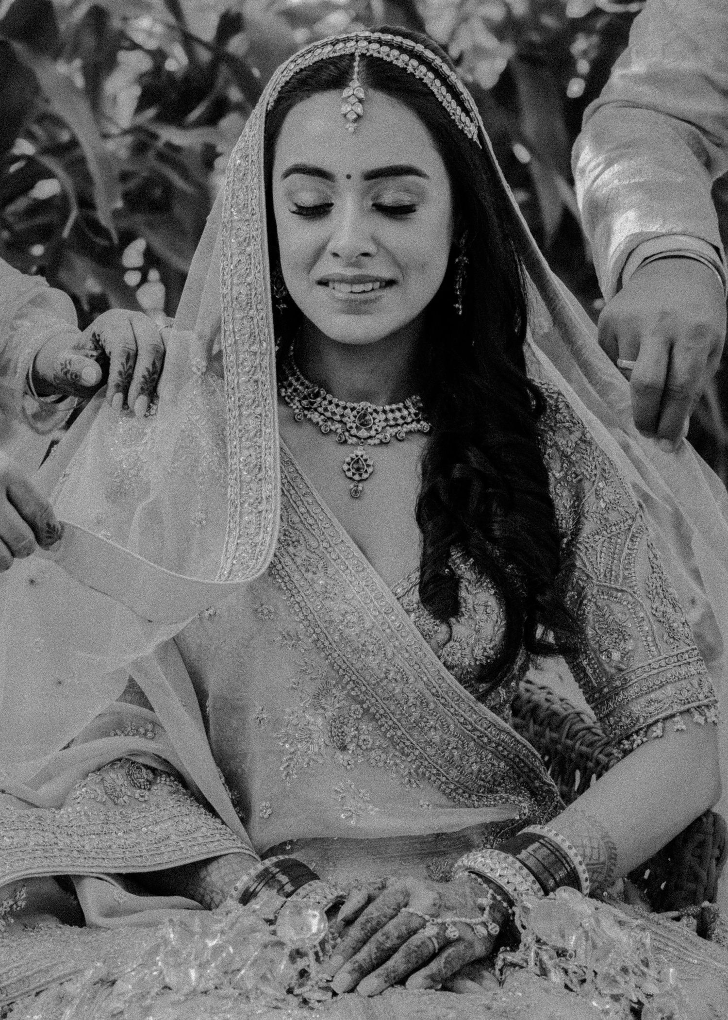 A monochrome image of a bride in traditional Indian attire with detailed jewelry and veil.