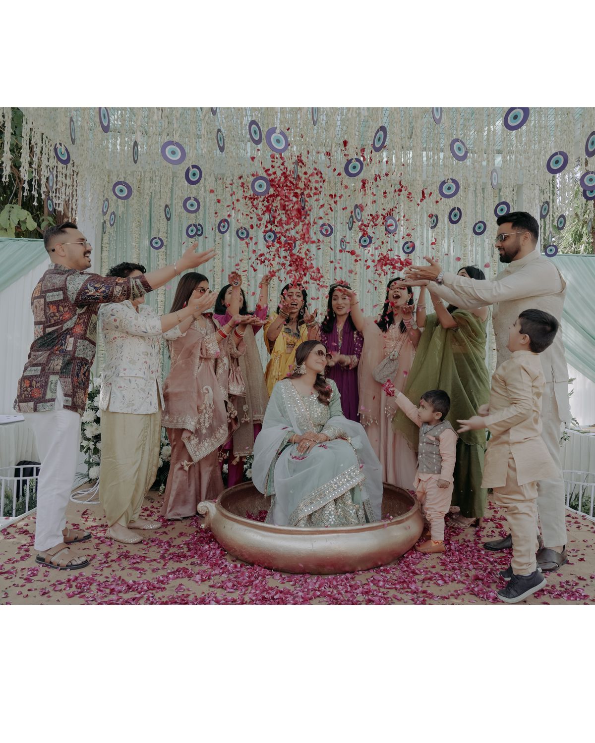 Wedding party gathers around seated bride for festive rose petal shower celebration.