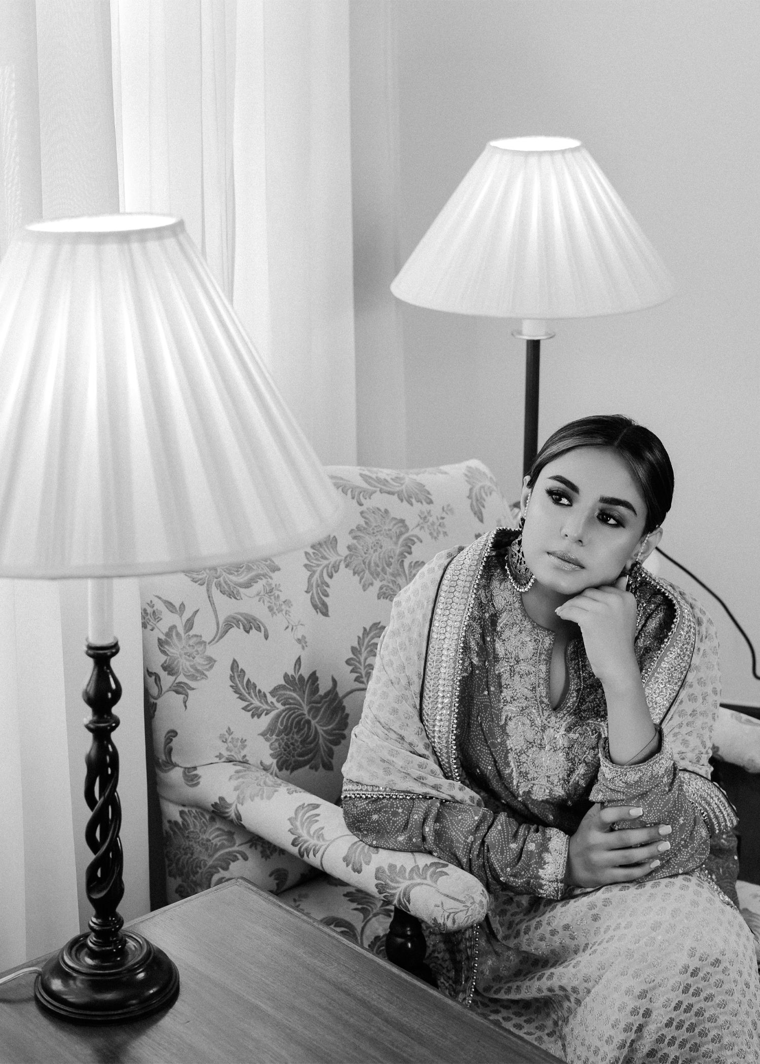 Black and white photo showing floral wallpaper, two traditional table lamps with pleated shades and traditional decor.
