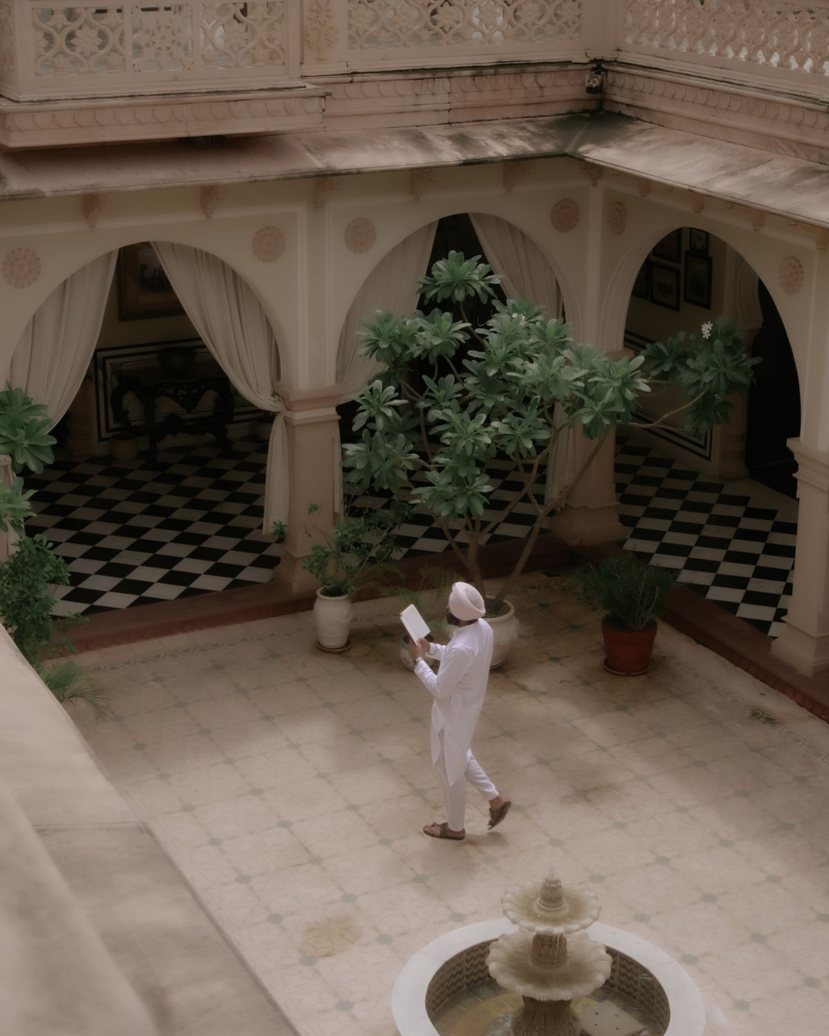Aerial view of courtyard with fountain and person in white walking among potted plants.