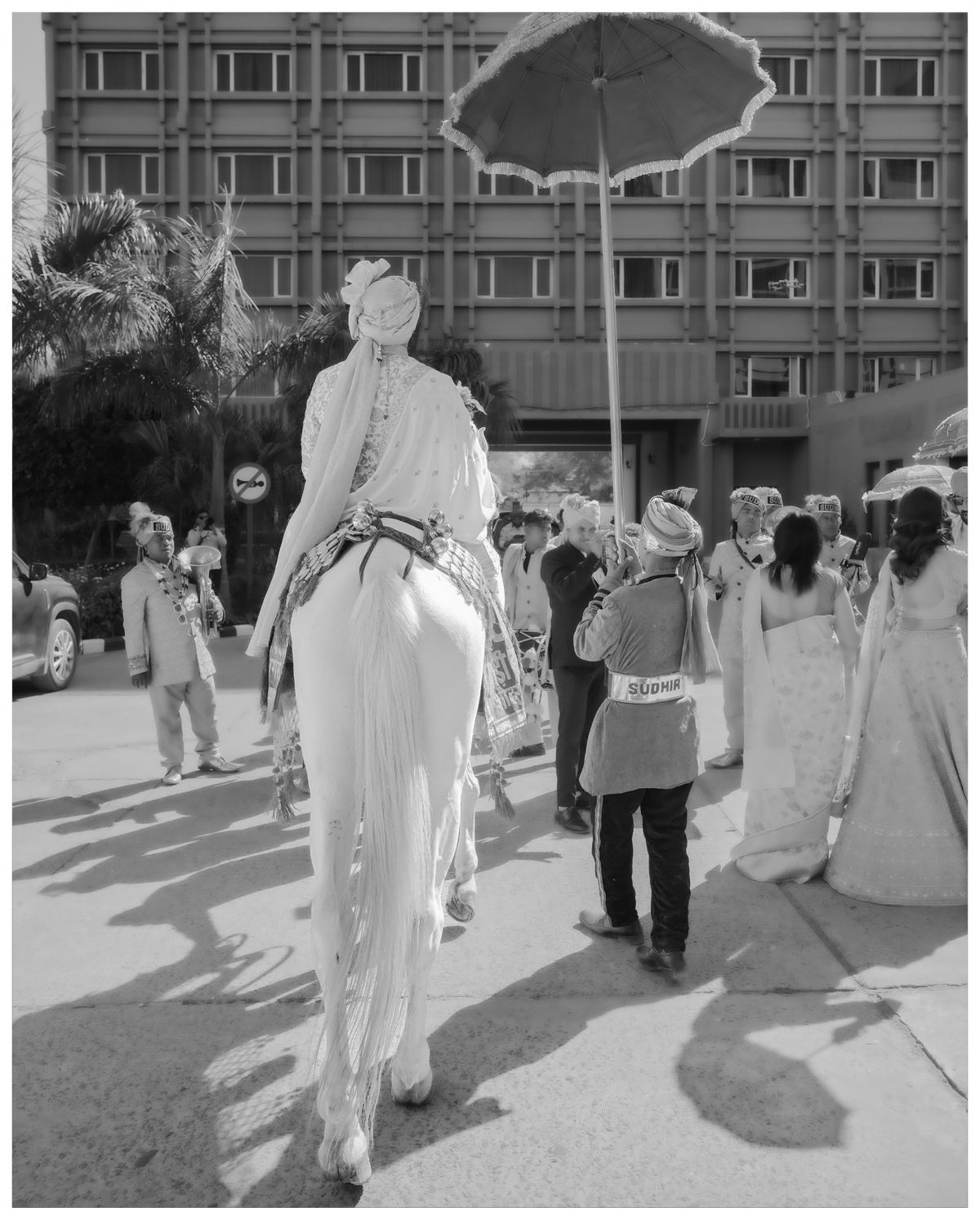 Black and white photo of a street celebration with people gathered around someone on stilts.