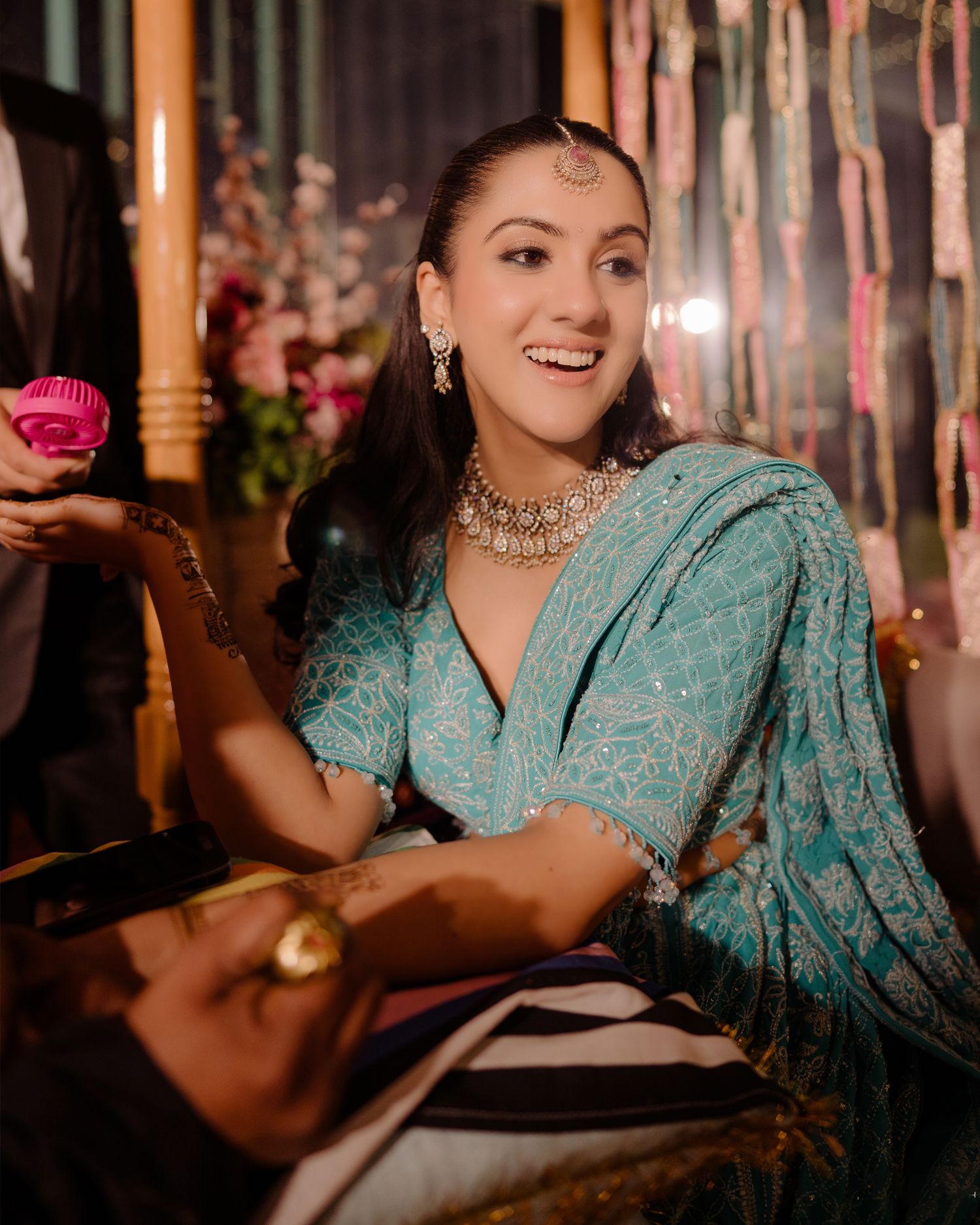 Smiling woman in teal embroidered saree with kundan jewelry and maang tikka at an Indian celebration.