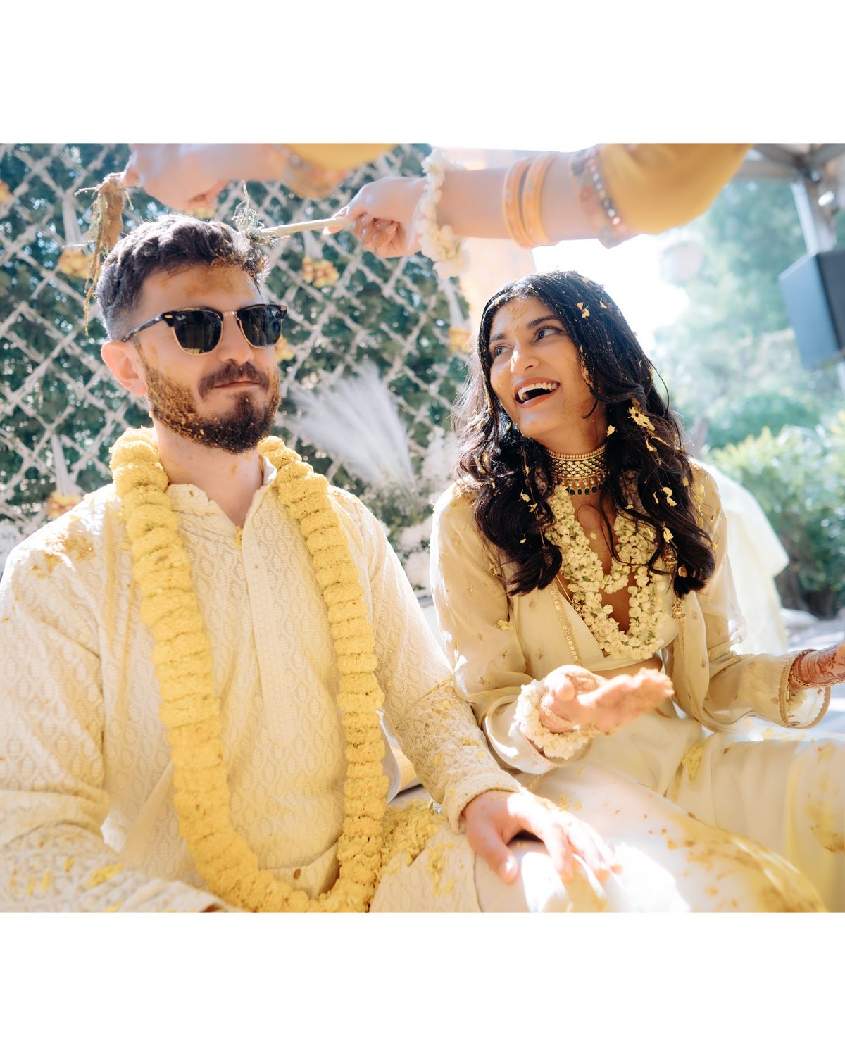 Couple shares a lighthearted moment at outdoor celebration wearing matching cream and yellow attire.