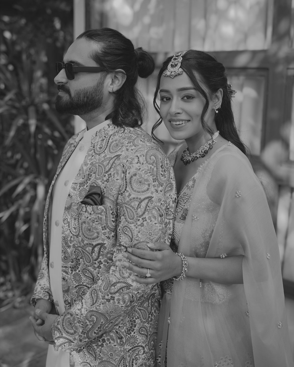 Black and white portrait of a couple in traditional South Asian wedding attire with intricate embroidery and jewelry.