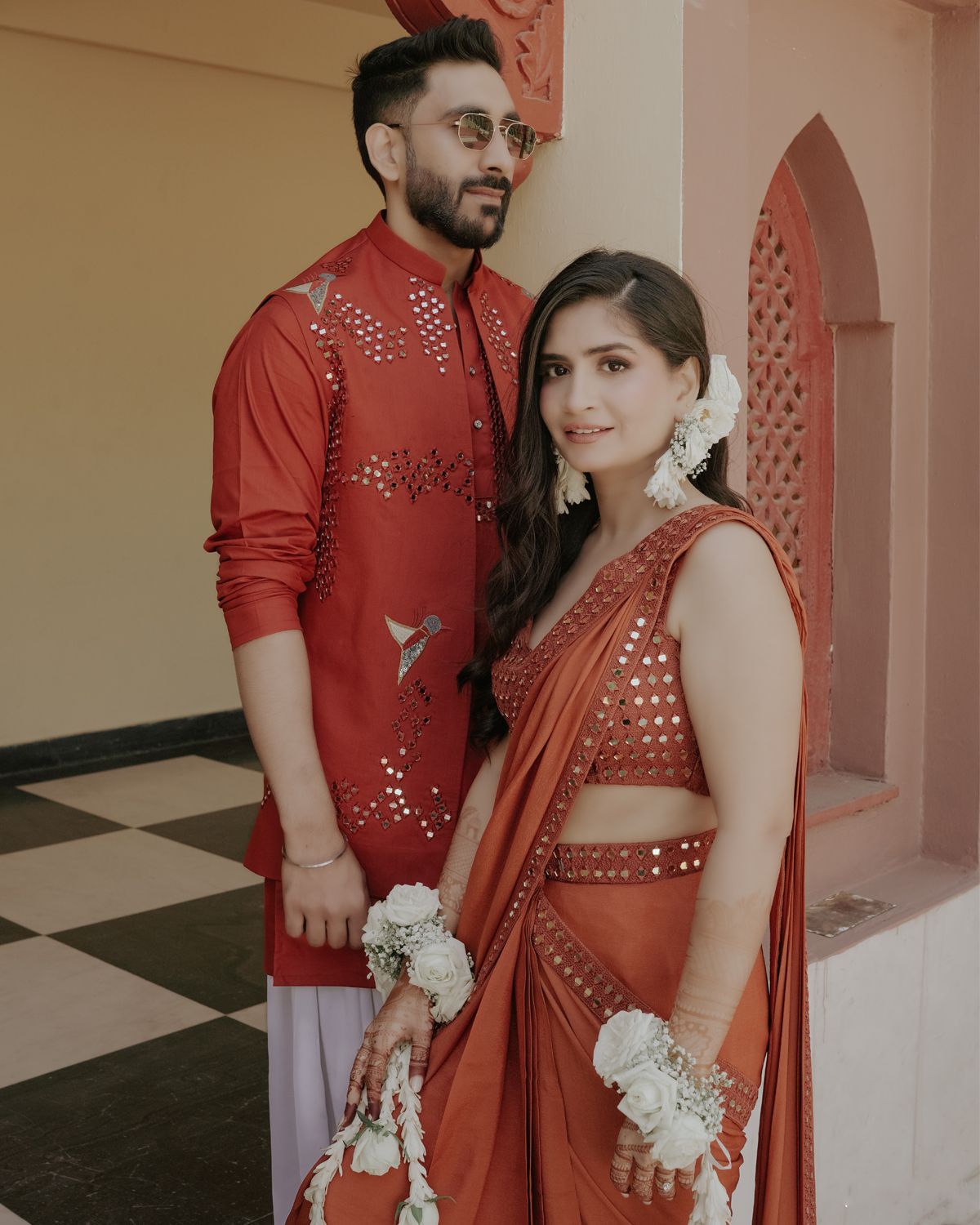 Couple wearing matching red traditional Indian outfits with detailed embroidery.