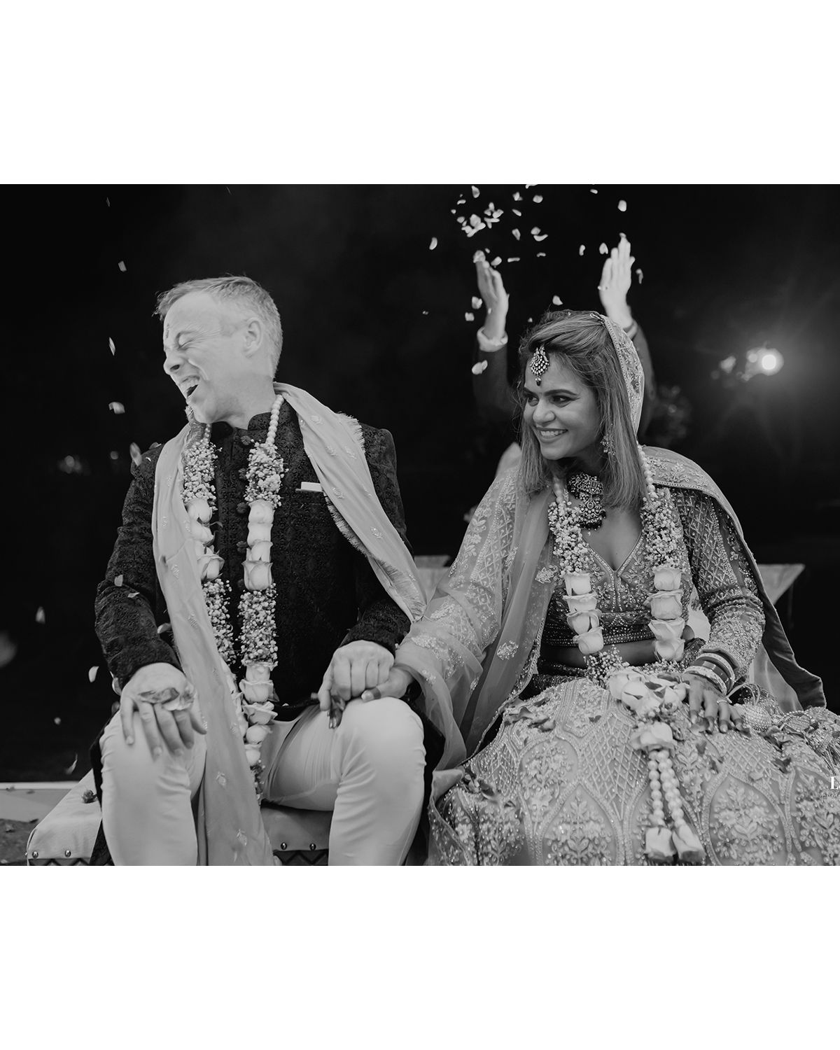 Black and white photo of a couple in wedding attire with confetti falling around them.
