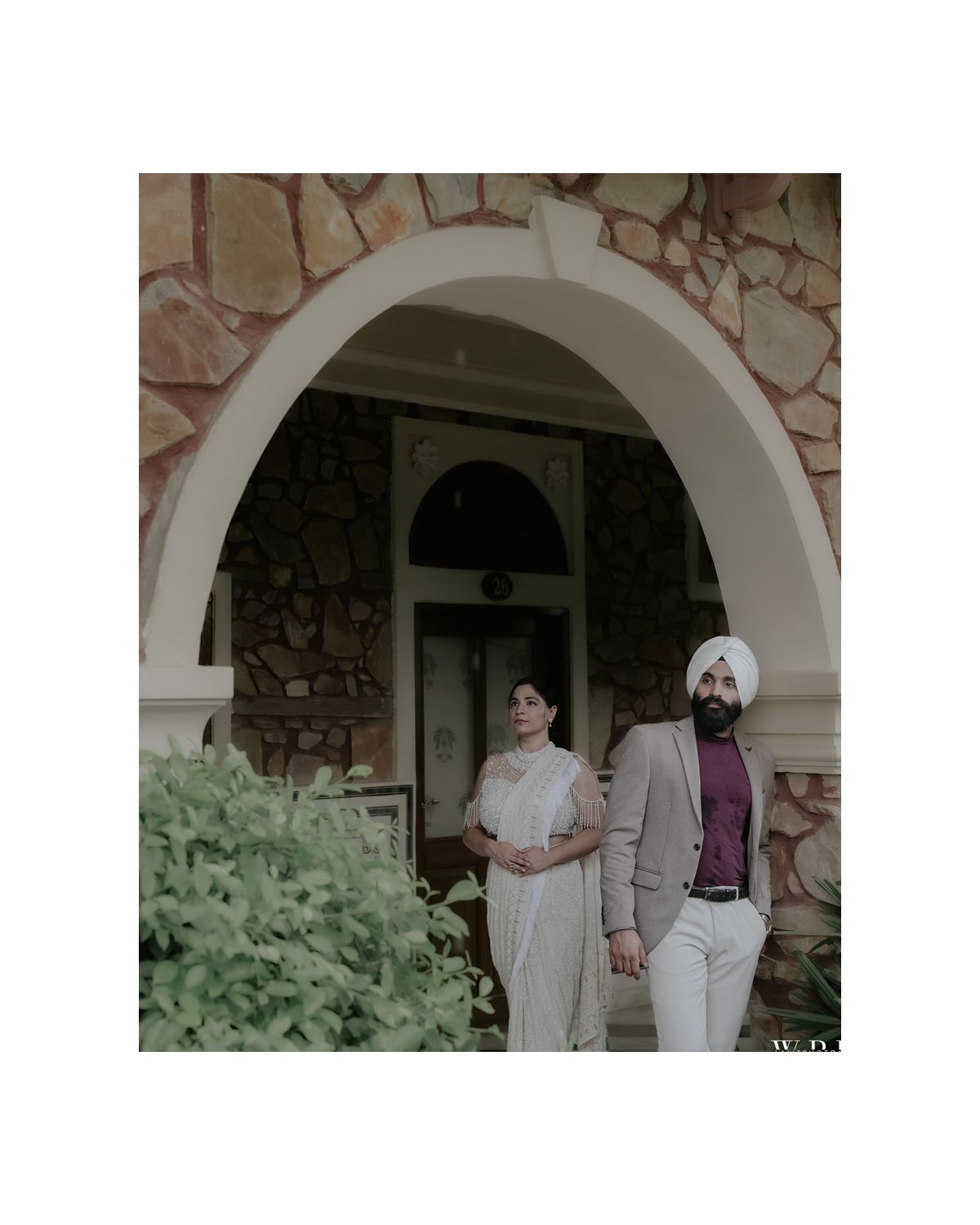 Couple poses elegantly at a stone archway entrance with vintage aesthetic and decorative greenery.