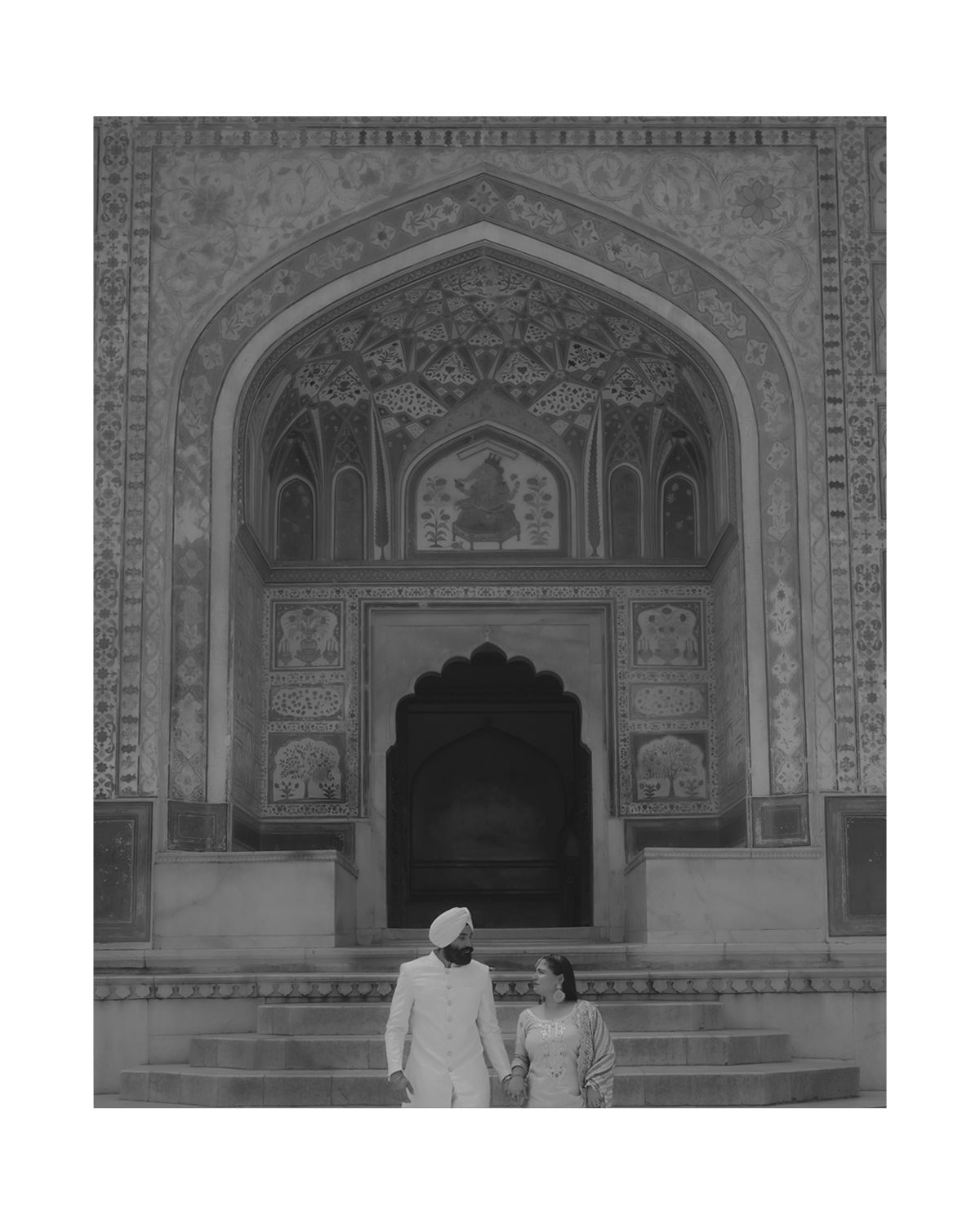 Two people viewing an elaborately decorated entrance arch with Islamic geometric patterns and designs.