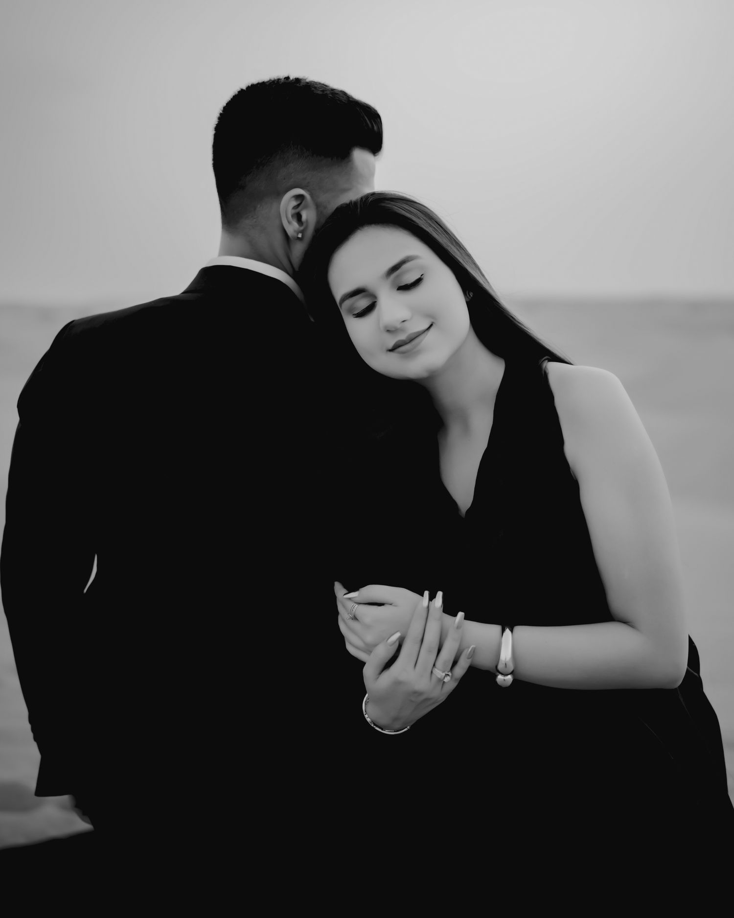 Black and white photo of a couple in elegant attire sharing a tender moment, woman resting her head on mans shoulder.