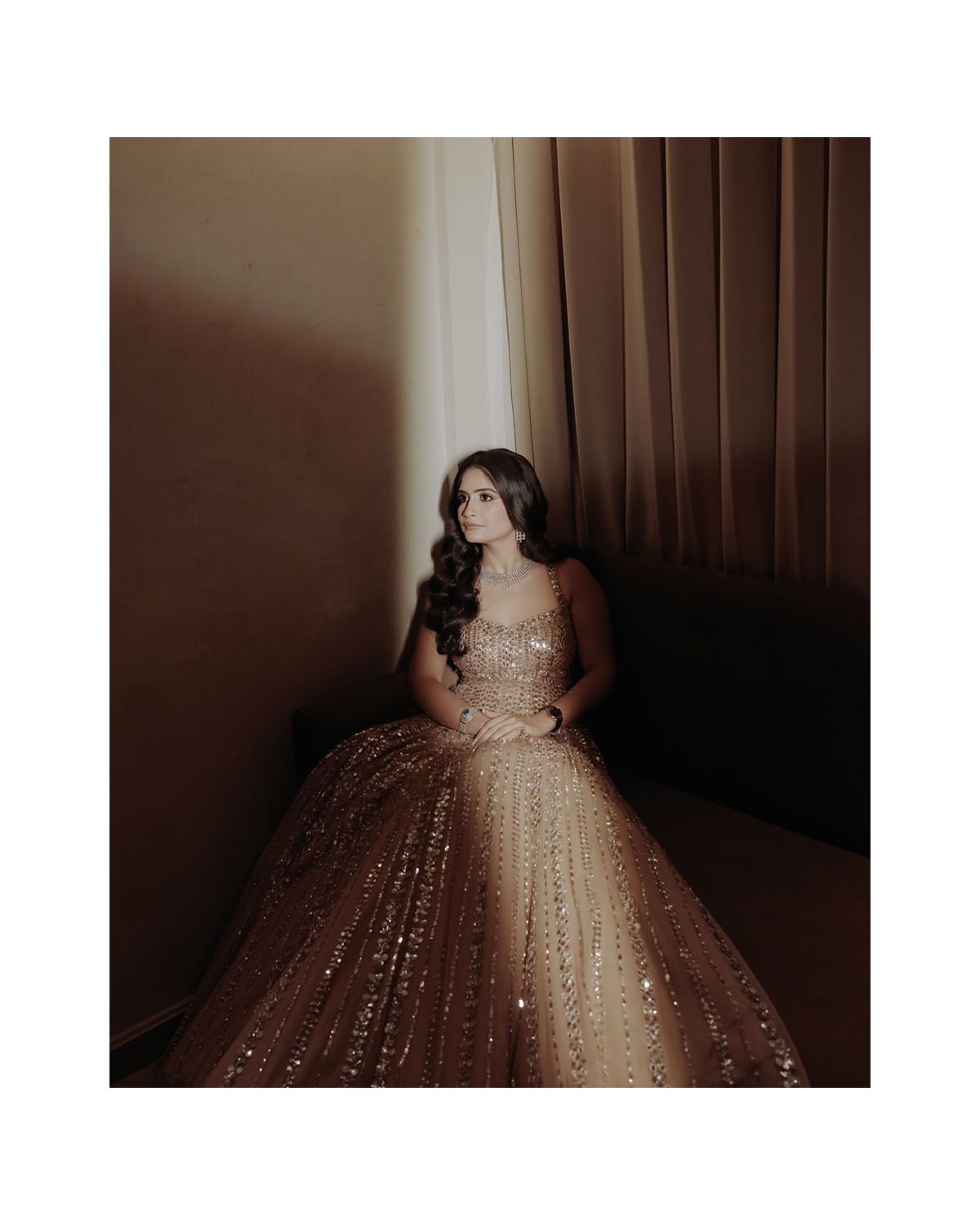 Woman in a glittering ball gown poses in dramatic lighting against dark curtains.