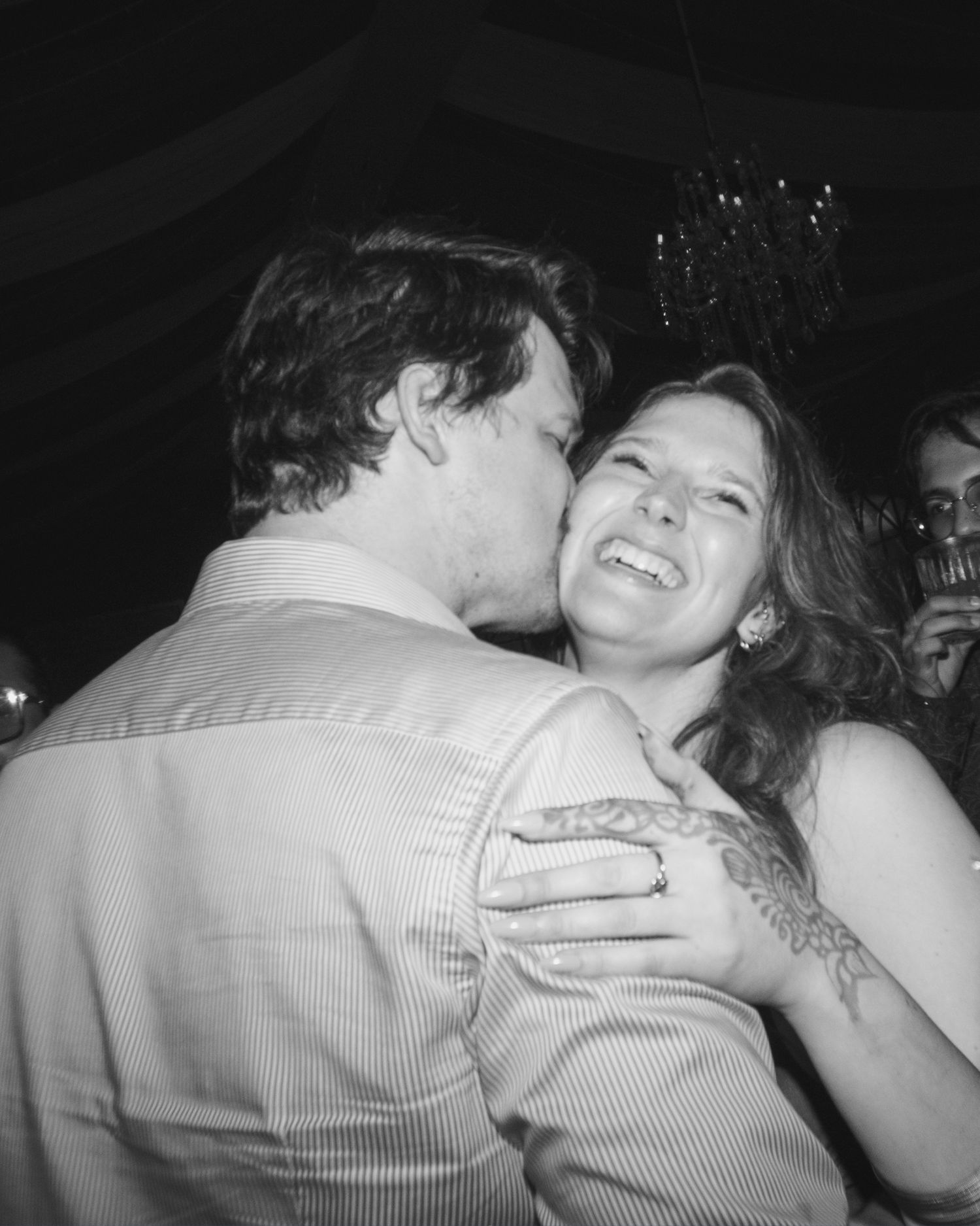 Black and white photo of a couple sharing a romantic kiss and embrace at a wedding reception.