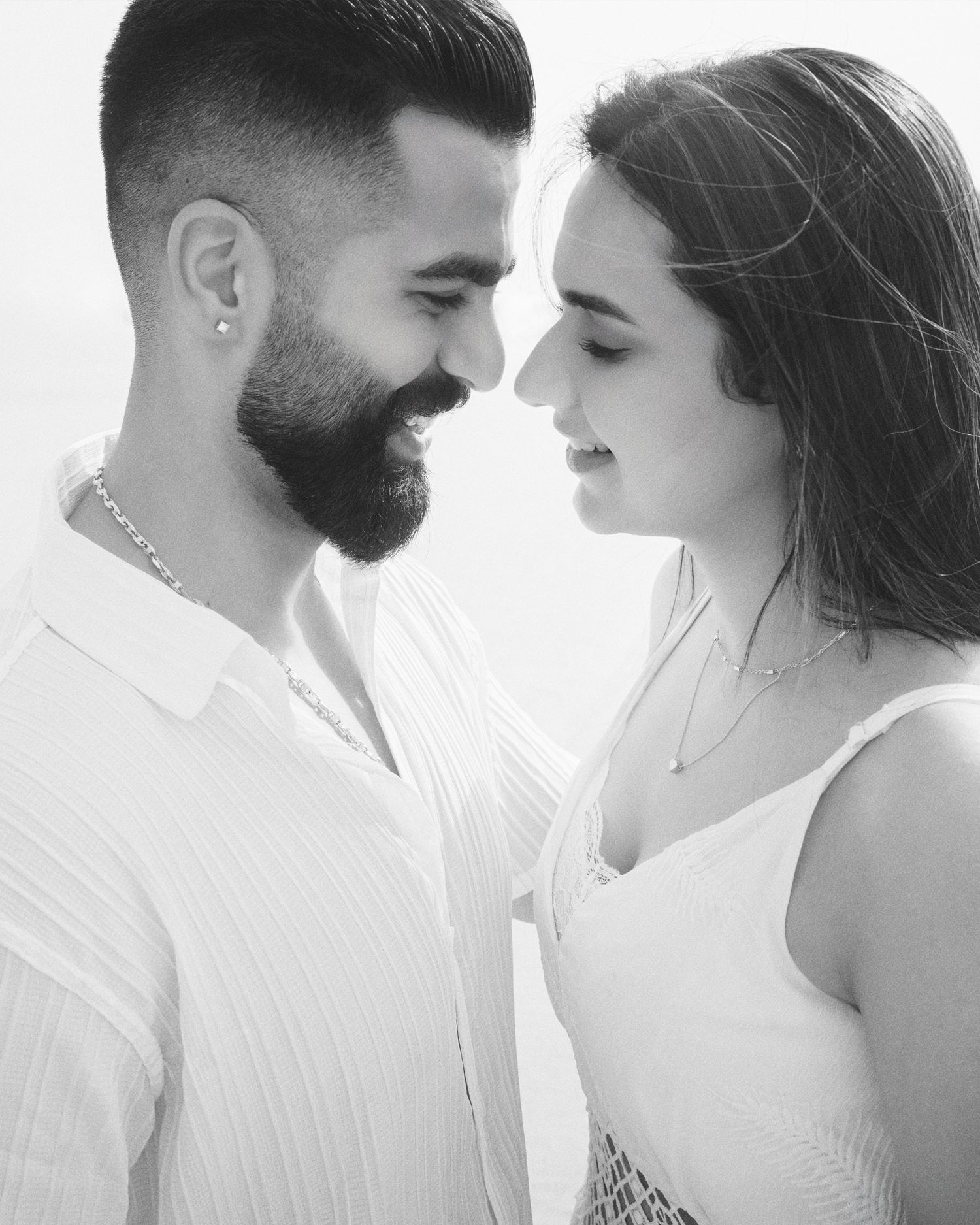 Black and white photo of a romantic couple in white outfits facing each other closely, sharing an intimate moment.