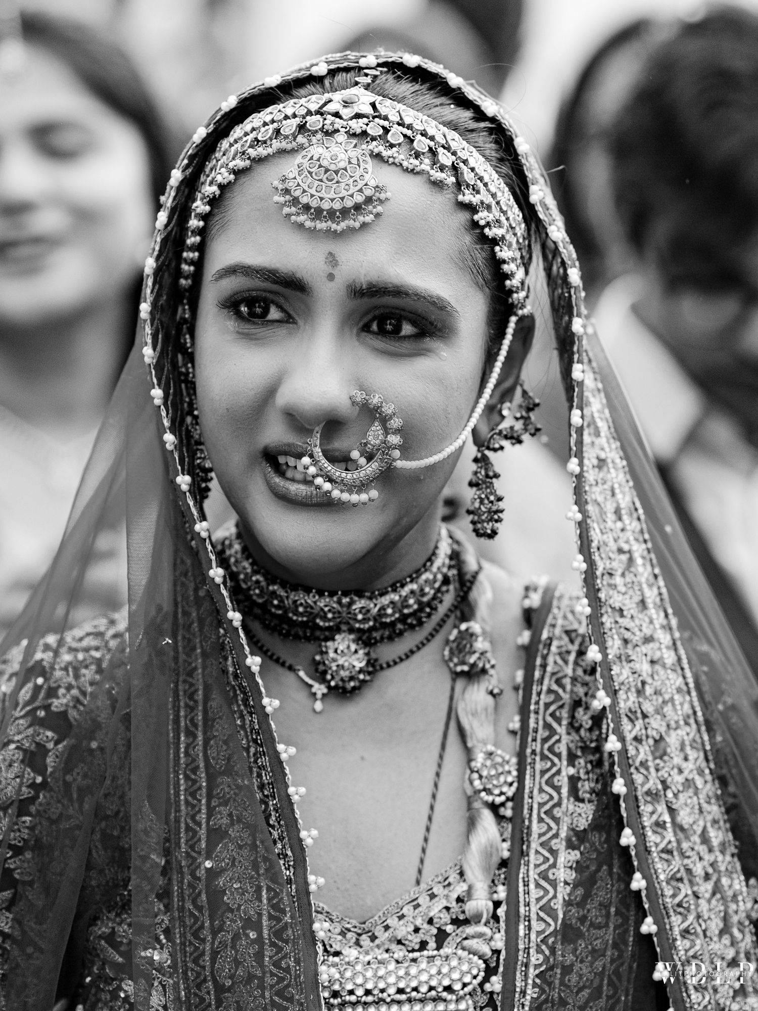 Black and white portrait of an Indian bride in traditional bridal jewelry, maang tikka, nose ring, and embroidered veil.