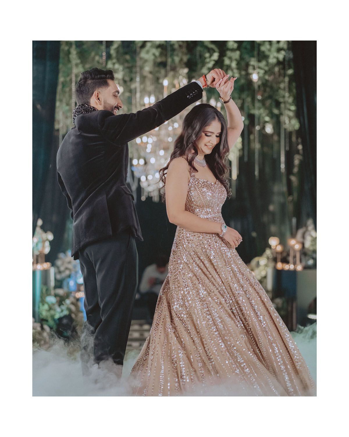 Couple dancing at elegant event with man twirling woman in sparkly champagne gown.
