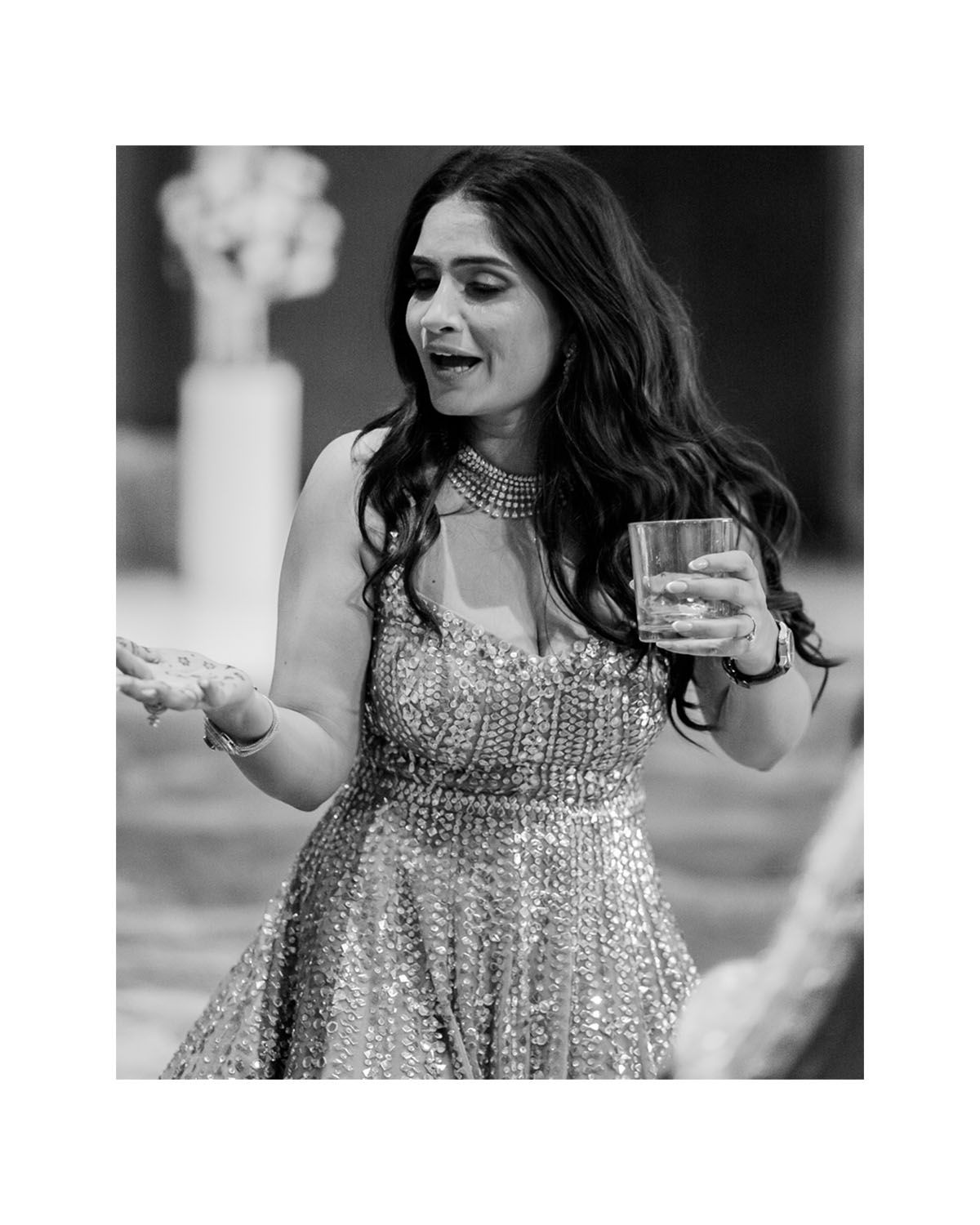 Woman in sparkly formal dress dancing and holding a drink at a celebration.