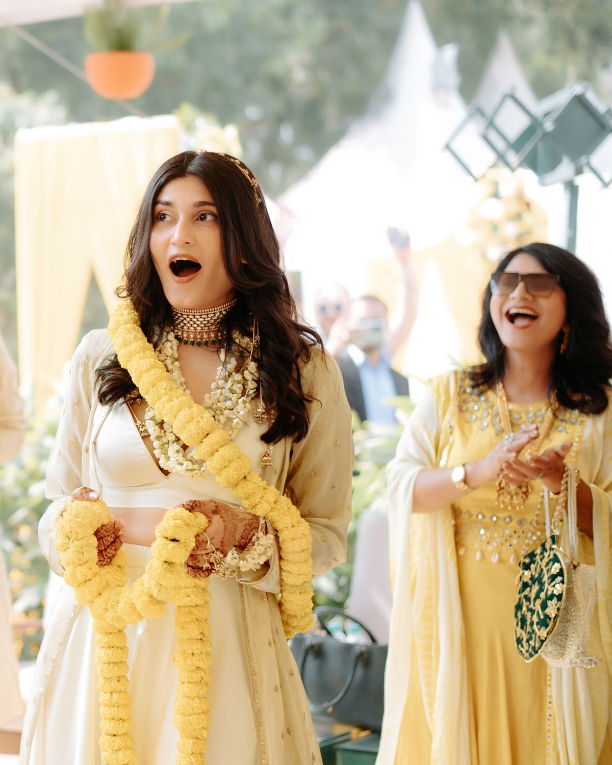 Two people in yellow and white traditional attire share excited expressions during a celebration.