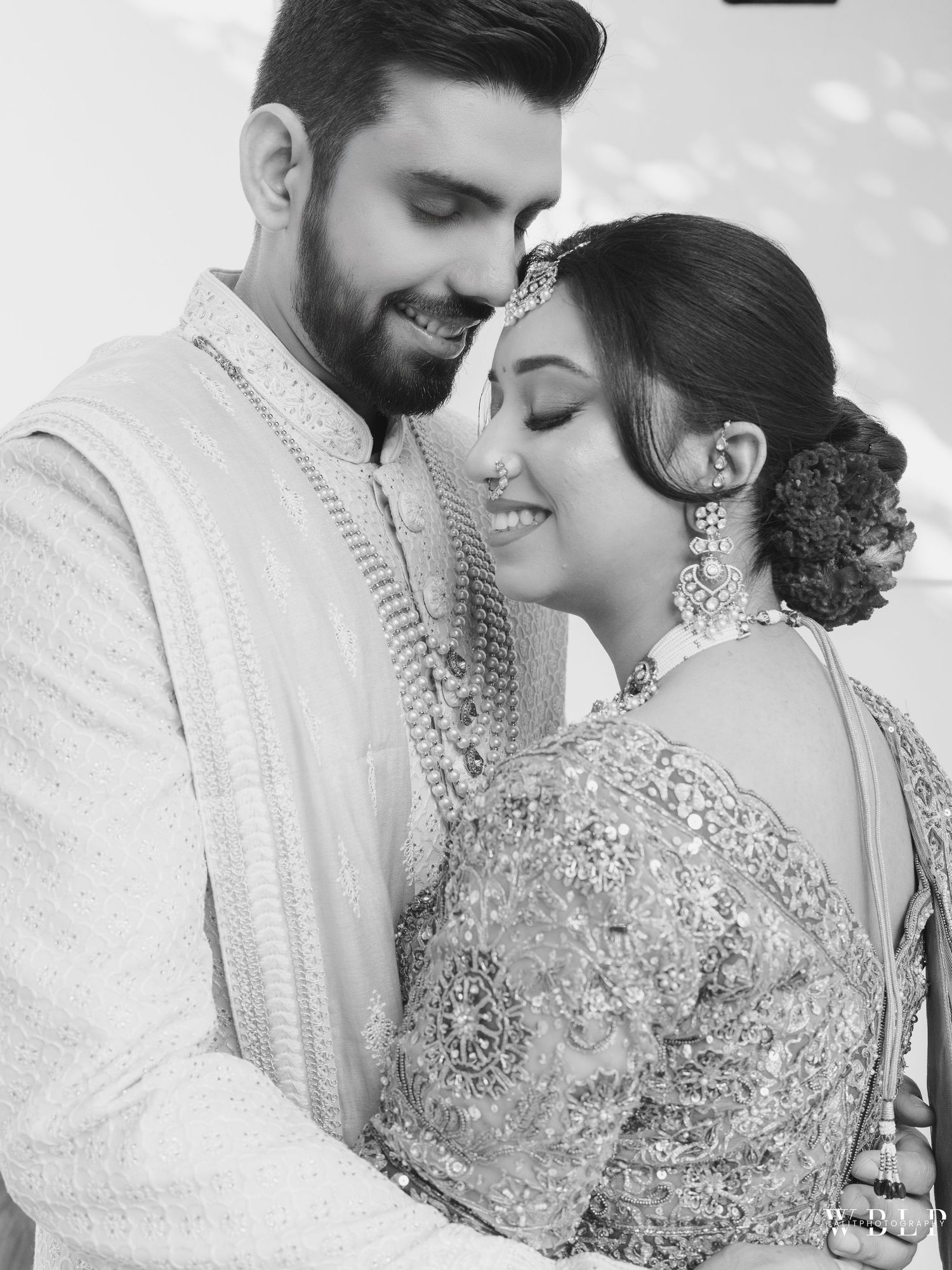Black and white photo of an Indian couple in traditional wedding attire, bride in embroidered lehenga with maang tikka.