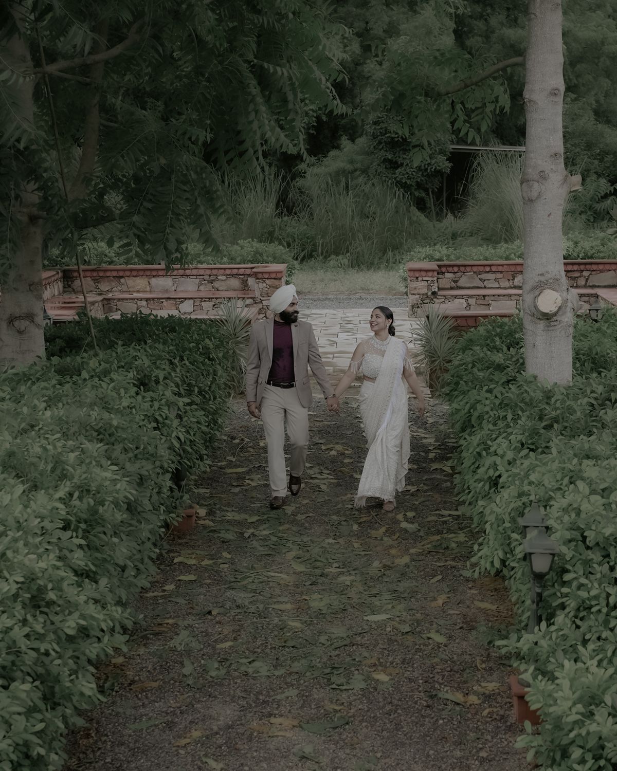 Couple strolls hand in hand along a garden path surrounded by lush greenery.