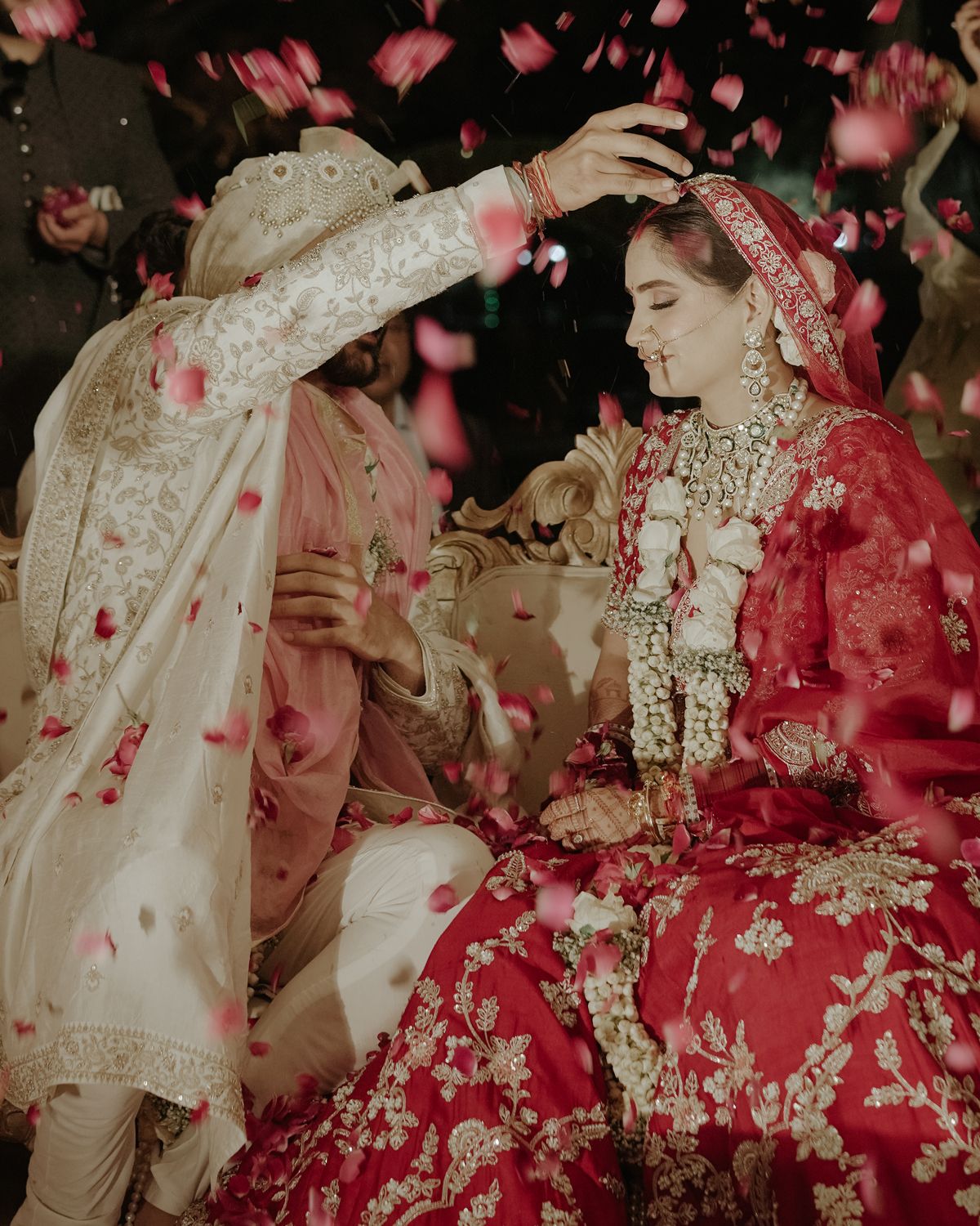 Traditional Indian wedding ceremony with flower petals falling and ornate red bridal lehenga.