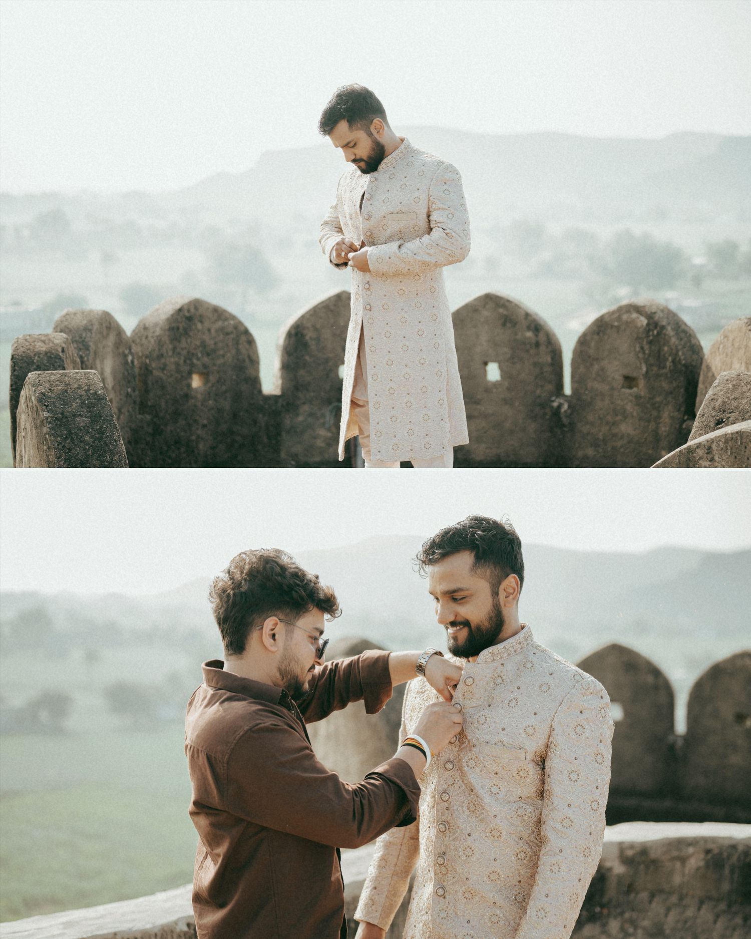 Groom in embroidered sherwani being helped by friend at historic fort with misty hills backdrop.