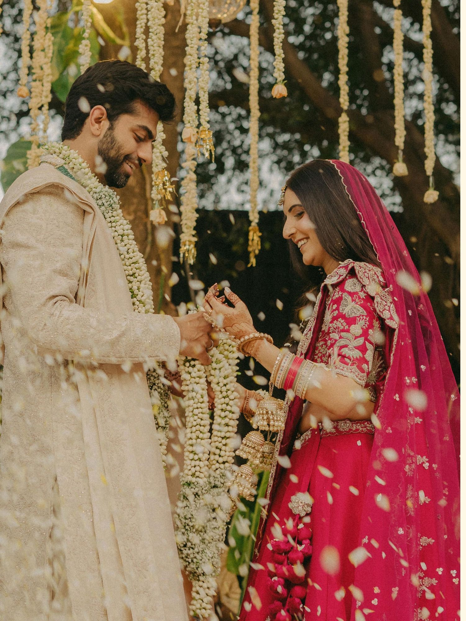 Indian couple exchanging garlands during traditional wedding ceremony, bride in pink lehenga, groom in beige sherwani.