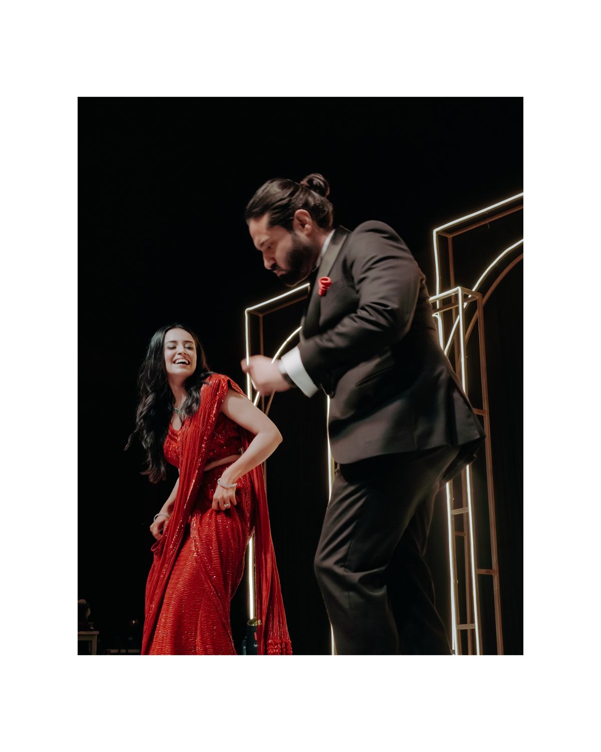 A couple performs an elegant dance pose on stage, with her in a stunning red dress and him in a dark suit.