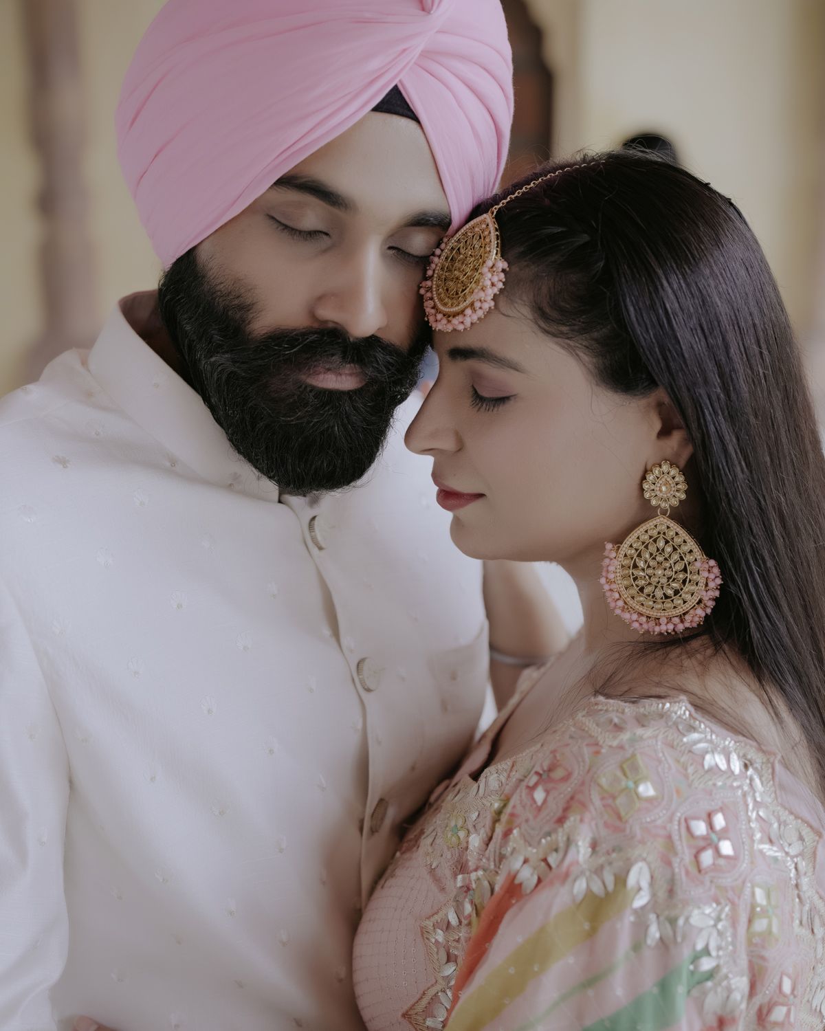Intimate portrait of a couple in traditional Punjabi wedding attire with detailed jewelry and soft lighting.