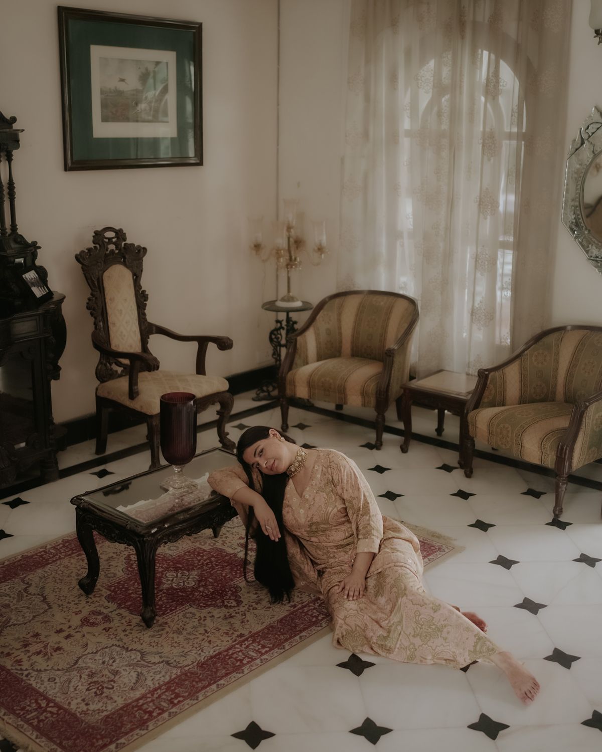 Dramatic portrait in vintage living room showing person reclining on ornate rug among classic furniture.