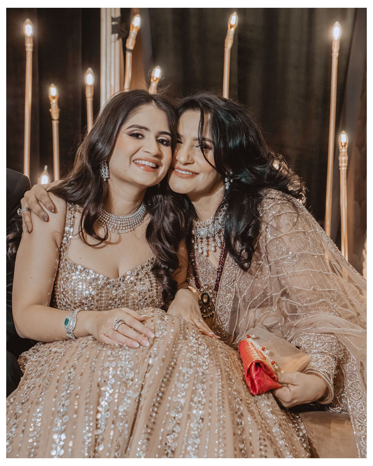 Two guests in shimmering outfits share a warm embrace during an elegant celebration.