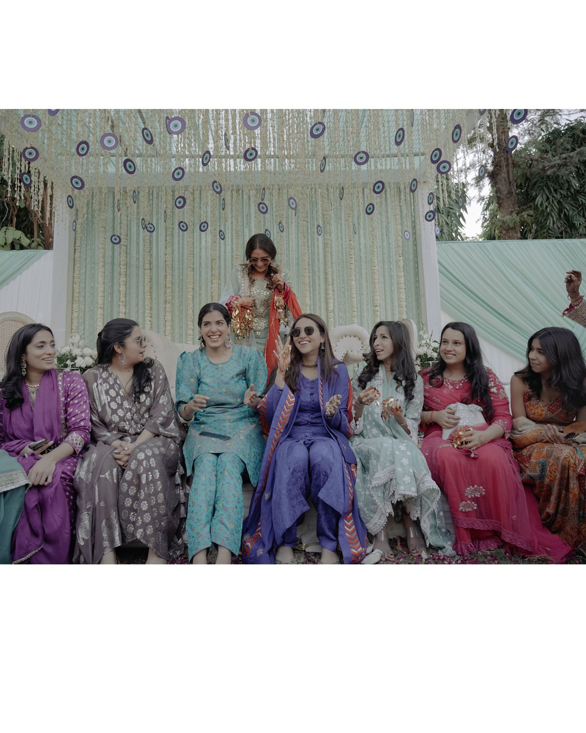 Group of guests in colorful traditional outfits seated at an outdoor wedding event.