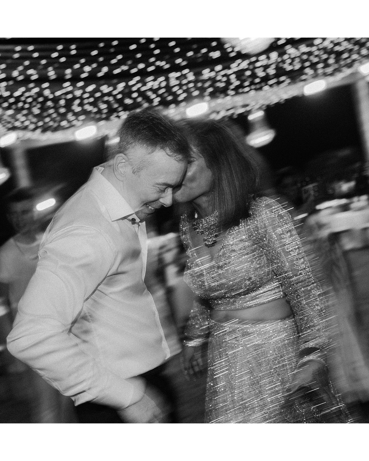 Couple dancing under twinkling lights at a wedding reception in black and white.