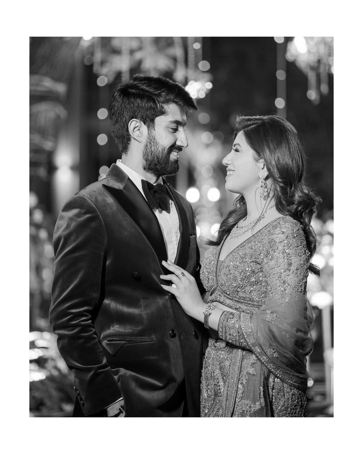 Black and white portrait of a couple in formal wear sharing an intimate moment under ambient lighting.