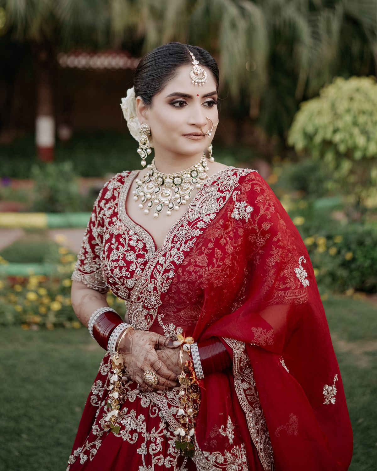 Close-up portrait showcasing intricate bridal jewelry and red embroidered lehenga details.
